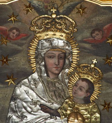 Zdjęcie nr 3: Obraz w kształcie stojącego prostokąta, zamkniętego łukiem wklęsło-wypukłym z uskokami, z wizerunkiem Matki Boskiej Śnieżnej. Maria przedstawiona frontalnie, w półpostaci, z Dzieciątkiem Jezus na lewym ręku, ze skrzyżowanymi dłońmi. Twarz podłużna z długim i wąskim nosem, drobnymi ustami, dużymi oczami obwiedzionymi regularnymi łukami brwiowymi, ze wzrokiem skierowanym wprost na widza. Dzieciątko zwrócone trzy czwarte w prawo, w pozycji siedzącej, z jabłkiem królewskim w lewej dłoni, prawą czyniące gest błogosławieństwa, na stopach ma założone sandałki. Twarz okrągła o wyrazistych rysach, duże i brązowe oczy, zarumienione policzki, włosy średniej długości opadające na plecy, wzrok skierowany na Matkę. Tło w odcieniach szarości, w górnej części pochmurne niebo. Nad głową Marii gołębica Ducha Świętego z kwiatem róży w dziobie. W górnych narożach dwie przeciwstawnie ustawione, uskrzydlone główki aniołków. Na postacie Marii i Dzieciątka nałożone metalowe sukienki, promieniste nimby, korony w typie zamkniętym i wieniec z 12 gwiazd wokół głów.
