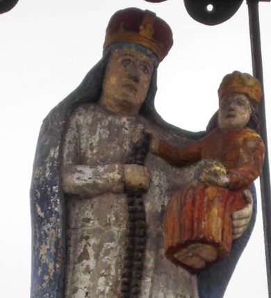 Zdjęcie nr 1: Kapliczka wolnostojąca z postacią Matki Boskiej Różańcowej na wysokim cokole. Podstawa podzielona na trzy strefy – dolna na uskokowym cokole z płyciną w kształcie leżącego prostokąta o wklęsłych narożach, wyższa z tablicą z kutym, złoconym napisem „BĄDŹ / POZDRO/WIONA / KRÓLOWA / NIEBIESKA / ROKU PAN(SKIEGO) / 1822”, najwyższa gładka. Całość ujęta spływami wolutowymi i zwieńczona belkowaniem przechodzącym na osi w łuk nadwieszony z wpisaną palmetą. Na cokole figura Matki Boskiej ukazanej całopostaciowo, frontalnie z Dzieciątkiem na lewym ramieniu, prawą ręką trzyma ujęty przez nie różaniec. Obie postaci mają na głowie zamknięte korony. Maria jest ubrana w białą suknię i niebieski płaszcz, Dzieciątko w czerwoną sukienkę. Postacie przykrywa metalowy daszek wsparty na czterech prętach. 