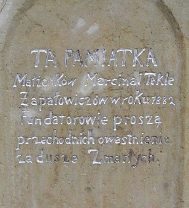 Zdjęcie nr 4: Kapliczka wolnostojąca z figurą św. Floriana na wysokim, dwustrefowym cokole. Dolna część prostopadłościenna, na profilowanej podstawie, z płytką niszą w kształcie stojącego prostokąta zamkniętego łukiem pełnym na każdej ścianie. Na froncie napis „TA PAMIATKA / Małżonków Marcina i Telke / Zapałowiczów w roku 1882 / Fundatorowie proszą / przechodnich o westchnienie / za dusze Zmarłych”. Na bocznych ścianach płaskorzeźbione postacie świętych ukazanych w całej postaci, frontalnie. Z jednej strony wizerunek  świętej męczennicy z płonącą budowlą z lewej strony i psem/smokiem z prawej (św. Małgorzata?). Święta trzyma w prawej ręce palmę męczeństwa, lewą przyciska do piersi. Ma łagodną, owalną twarz, włosy z przedziałkiem, zaczesane do tyłu. Jest ubrana w czerwoną, przepasaną suknię i czerwony płaszcz.  Na innej płaszczyźnie postać św. Andrzeja przedstawionego jako brodaty mężczyzna w niebieskiej tunice i czerwonym płaszczu. Za jego plecami widać końce ramion krzyża w kształcie litery „X”. Na kolejnej św. Jan Nepomucen w sutannie, komży i płaszczu, w birecie. Z krucyfiksem i palmą męczeństwa w rękach. Na kolejnej ściance św. Marcin na koniu, w stroju żołnierza, trzymanym w prawej ręce mieczem odcina część płaszcza, który chwyta siedząca na ziemi postać w czerwonych spodniach i zielonej koszuli. W górnej strefie cokołu, w ścianie frontowej nisza z figurą Matki Boskiej w całej postaci, frontalnie, z rękami złożonymi do modlitwy i różańcem. Maria ma na sobie białą suknię i niebieski płaszcz zarzucony na głowę; na bosych stopach kwiaty róż Na cokole postać św. Floriana w całej postaci, frontalnie, z cebrzykiem z którego leje się woda na płonący dom w prawej i włócznią w lewej ręce. Ma owalną twarz, wąsy i brodę. Ubrany jest w strój rzymskiego legionisty – jasną tunikę, czerwony płaszcz, wysokie buty i hełm.