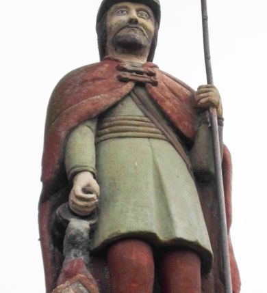 Zdjęcie nr 11: Kapliczka wolnostojąca z figurą św. Floriana na wysokim, dwustrefowym cokole. Dolna część prostopadłościenna, na profilowanej podstawie, z płytką niszą w kształcie stojącego prostokąta zamkniętego łukiem pełnym na każdej ścianie. Na froncie napis „TA PAMIATKA / Małżonków Marcina i Telke / Zapałowiczów w roku 1882 / Fundatorowie proszą / przechodnich o westchnienie / za dusze Zmarłych”. Na bocznych ścianach płaskorzeźbione postacie świętych ukazanych w całej postaci, frontalnie. Z jednej strony wizerunek  świętej męczennicy z płonącą budowlą z lewej strony i psem/smokiem z prawej (św. Małgorzata?). Święta trzyma w prawej ręce palmę męczeństwa, lewą przyciska do piersi. Ma łagodną, owalną twarz, włosy z przedziałkiem, zaczesane do tyłu. Jest ubrana w czerwoną, przepasaną suknię i czerwony płaszcz.  Na innej płaszczyźnie postać św. Andrzeja przedstawionego jako brodaty mężczyzna w niebieskiej tunice i czerwonym płaszczu. Za jego plecami widać końce ramion krzyża w kształcie litery „X”. Na kolejnej św. Jan Nepomucen w sutannie, komży i płaszczu, w birecie. Z krucyfiksem i palmą męczeństwa w rękach. Na kolejnej ściance św. Marcin na koniu, w stroju żołnierza, trzymanym w prawej ręce mieczem odcina część płaszcza, który chwyta siedząca na ziemi postać w czerwonych spodniach i zielonej koszuli. W górnej strefie cokołu, w ścianie frontowej nisza z figurą Matki Boskiej w całej postaci, frontalnie, z rękami złożonymi do modlitwy i różańcem. Maria ma na sobie białą suknię i niebieski płaszcz zarzucony na głowę; na bosych stopach kwiaty róż Na cokole postać św. Floriana w całej postaci, frontalnie, z cebrzykiem z którego leje się woda na płonący dom w prawej i włócznią w lewej ręce. Ma owalną twarz, wąsy i brodę. Ubrany jest w strój rzymskiego legionisty – jasną tunikę, czerwony płaszcz, wysokie buty i hełm.