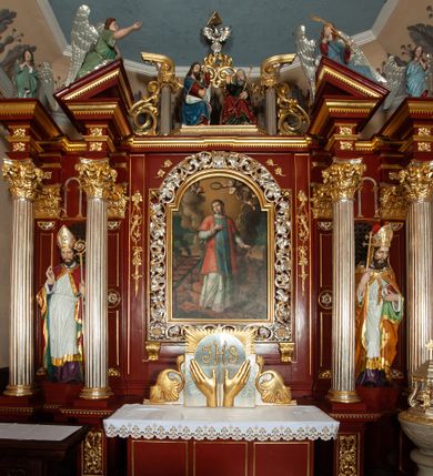 Zdjęcie nr 1: Ołtarz architektoniczny, trójosiowy, jednokondygnacyjny ze zwieńczeniem, na cokole. Mensa prostopadłościenna, drewniana, z portatylem. Antepedium na profilowanej podstawie podzielone na trzy bliskie kwadratom płyciny. Metalowe tabernakulum w formie prostopadłościanu ujętego wolutami z liści. Na ścianie frontowej drzwiczki dekorowane hostią z literami IHS ujętą od dołu rozłożonymi dłońmi.  Osie nastawy wydzielone dwiema parami pilastrów i stojącymi przed licem ołtarza kolumnami z kapitelami kompozytowymi. Wewnętrzna para kolumn dźwiga imposty z przerwanym przyczółkiem, na którym siedzi para klęczących aniołów, zaś zewnętrzna para dźwiga imposty z aniołami półleżącymi. Pole środkowe tworzy szeroka, wypełniona ażurowym akantem i rozetami rama w formie stojącego prostokąta zamkniętego łukiem nadwieszonym, ujęta lizenami, podtrzymywana przez konsole, z obrazem św. Wawrzyńca wymiennie z obrazem św. Józefa oraz rzeźbionym krucyfiksem. W osiach bocznych figury św. Stanisława po lewej i św. Wojciecha po prawej stronie, na tle arkad z ażurową kratką. Zwieńczenie tworzy grupa rzeźbiarska z przedstawieniem Trójcy Świętej. Bóg Ojciec i Chrystus siedzą zwróceni do siebie, na tle ulistionych wolut, które podtrzymują gołębicę Ducha Świetego, nad którą unosi się Oko Opatrzności. Grupa jest flankowana przez jońskie kolumny ze zwróconymi na zewnątrz wolutami, ujęta fragmentami wici tworzącymi spływy wolutowe. Cokoły kolumn dekorowane płycinami z akantem, rozetą i liliami heraldycznymi, zwieńczone ząbkowaniem. W przyłuczach dekoracja roślinna. Płycinę lizen zdobią festony z wstęgą regencyjną. Trzony pilastrów podzielone na dwie płyciny o wklęsłych bokach, dekorowane rozetami. Architrawy i fryzy dekorowane rozetami z akantu, gzyms z ząbkowaniem. Kolumny zwieńczenia dekorowane akantowymi spływami wolutowymi. Ołtarz polichromowany na ciemnoczerwono; ornamentyka oraz detale architektoniczne złocone i srebrzone. 