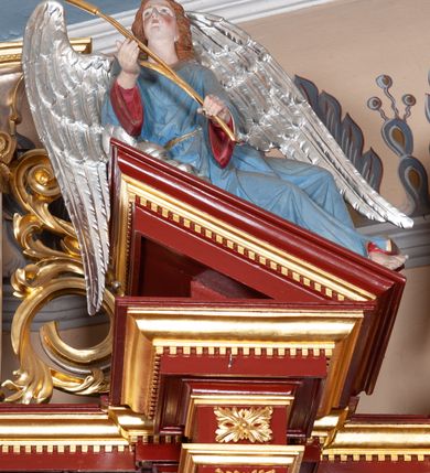 Zdjęcie nr 39: Ołtarz architektoniczny, trójosiowy, jednokondygnacyjny ze zwieńczeniem, na cokole. Mensa prostopadłościenna, drewniana, z portatylem. Antepedium na profilowanej podstawie podzielone na trzy bliskie kwadratom płyciny. Metalowe tabernakulum w formie prostopadłościanu ujętego wolutami z liści. Na ścianie frontowej drzwiczki dekorowane hostią z literami IHS ujętą od dołu rozłożonymi dłońmi.  Osie nastawy wydzielone dwiema parami pilastrów i stojącymi przed licem ołtarza kolumnami z kapitelami kompozytowymi. Wewnętrzna para kolumn dźwiga imposty z przerwanym przyczółkiem, na którym siedzi para klęczących aniołów, zaś zewnętrzna para dźwiga imposty z aniołami półleżącymi. Pole środkowe tworzy szeroka, wypełniona ażurowym akantem i rozetami rama w formie stojącego prostokąta zamkniętego łukiem nadwieszonym, ujęta lizenami, podtrzymywana przez konsole, z obrazem św. Wawrzyńca wymiennie z obrazem św. Józefa oraz rzeźbionym krucyfiksem. W osiach bocznych figury św. Stanisława po lewej i św. Wojciecha po prawej stronie, na tle arkad z ażurową kratką. Zwieńczenie tworzy grupa rzeźbiarska z przedstawieniem Trójcy Świętej. Bóg Ojciec i Chrystus siedzą zwróceni do siebie, na tle ulistionych wolut, które podtrzymują gołębicę Ducha Świetego, nad którą unosi się Oko Opatrzności. Grupa jest flankowana przez jońskie kolumny ze zwróconymi na zewnątrz wolutami, ujęta fragmentami wici tworzącymi spływy wolutowe. Cokoły kolumn dekorowane płycinami z akantem, rozetą i liliami heraldycznymi, zwieńczone ząbkowaniem. W przyłuczach dekoracja roślinna. Płycinę lizen zdobią festony z wstęgą regencyjną. Trzony pilastrów podzielone na dwie płyciny o wklęsłych bokach, dekorowane rozetami. Architrawy i fryzy dekorowane rozetami z akantu, gzyms z ząbkowaniem. Kolumny zwieńczenia dekorowane akantowymi spływami wolutowymi. Ołtarz polichromowany na ciemnoczerwono; ornamentyka oraz detale architektoniczne złocone i srebrzone. 