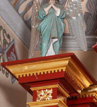 Zdjęcie nr 37: Ołtarz architektoniczny, trójosiowy, jednokondygnacyjny ze zwieńczeniem, na cokole. Mensa prostopadłościenna, drewniana, z portatylem. Antepedium na profilowanej podstawie podzielone na trzy bliskie kwadratom płyciny. Metalowe tabernakulum w formie prostopadłościanu ujętego wolutami z liści. Na ścianie frontowej drzwiczki dekorowane hostią z literami IHS ujętą od dołu rozłożonymi dłońmi.  Osie nastawy wydzielone dwiema parami pilastrów i stojącymi przed licem ołtarza kolumnami z kapitelami kompozytowymi. Wewnętrzna para kolumn dźwiga imposty z przerwanym przyczółkiem, na którym siedzi para klęczących aniołów, zaś zewnętrzna para dźwiga imposty z aniołami półleżącymi. Pole środkowe tworzy szeroka, wypełniona ażurowym akantem i rozetami rama w formie stojącego prostokąta zamkniętego łukiem nadwieszonym, ujęta lizenami, podtrzymywana przez konsole, z obrazem św. Wawrzyńca wymiennie z obrazem św. Józefa oraz rzeźbionym krucyfiksem. W osiach bocznych figury św. Stanisława po lewej i św. Wojciecha po prawej stronie, na tle arkad z ażurową kratką. Zwieńczenie tworzy grupa rzeźbiarska z przedstawieniem Trójcy Świętej. Bóg Ojciec i Chrystus siedzą zwróceni do siebie, na tle ulistionych wolut, które podtrzymują gołębicę Ducha Świetego, nad którą unosi się Oko Opatrzności. Grupa jest flankowana przez jońskie kolumny ze zwróconymi na zewnątrz wolutami, ujęta fragmentami wici tworzącymi spływy wolutowe. Cokoły kolumn dekorowane płycinami z akantem, rozetą i liliami heraldycznymi, zwieńczone ząbkowaniem. W przyłuczach dekoracja roślinna. Płycinę lizen zdobią festony z wstęgą regencyjną. Trzony pilastrów podzielone na dwie płyciny o wklęsłych bokach, dekorowane rozetami. Architrawy i fryzy dekorowane rozetami z akantu, gzyms z ząbkowaniem. Kolumny zwieńczenia dekorowane akantowymi spływami wolutowymi. Ołtarz polichromowany na ciemnoczerwono; ornamentyka oraz detale architektoniczne złocone i srebrzone. 