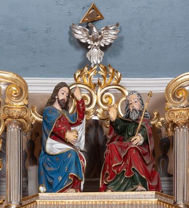 Zdjęcie nr 40: Ołtarz architektoniczny, trójosiowy, jednokondygnacyjny ze zwieńczeniem, na cokole. Mensa prostopadłościenna, drewniana, z portatylem. Antepedium na profilowanej podstawie podzielone na trzy bliskie kwadratom płyciny. Metalowe tabernakulum w formie prostopadłościanu ujętego wolutami z liści. Na ścianie frontowej drzwiczki dekorowane hostią z literami IHS ujętą od dołu rozłożonymi dłońmi.  Osie nastawy wydzielone dwiema parami pilastrów i stojącymi przed licem ołtarza kolumnami z kapitelami kompozytowymi. Wewnętrzna para kolumn dźwiga imposty z przerwanym przyczółkiem, na którym siedzi para klęczących aniołów, zaś zewnętrzna para dźwiga imposty z aniołami półleżącymi. Pole środkowe tworzy szeroka, wypełniona ażurowym akantem i rozetami rama w formie stojącego prostokąta zamkniętego łukiem nadwieszonym, ujęta lizenami, podtrzymywana przez konsole, z obrazem św. Wawrzyńca wymiennie z obrazem św. Józefa oraz rzeźbionym krucyfiksem. W osiach bocznych figury św. Stanisława po lewej i św. Wojciecha po prawej stronie, na tle arkad z ażurową kratką. Zwieńczenie tworzy grupa rzeźbiarska z przedstawieniem Trójcy Świętej. Bóg Ojciec i Chrystus siedzą zwróceni do siebie, na tle ulistionych wolut, które podtrzymują gołębicę Ducha Świetego, nad którą unosi się Oko Opatrzności. Grupa jest flankowana przez jońskie kolumny ze zwróconymi na zewnątrz wolutami, ujęta fragmentami wici tworzącymi spływy wolutowe. Cokoły kolumn dekorowane płycinami z akantem, rozetą i liliami heraldycznymi, zwieńczone ząbkowaniem. W przyłuczach dekoracja roślinna. Płycinę lizen zdobią festony z wstęgą regencyjną. Trzony pilastrów podzielone na dwie płyciny o wklęsłych bokach, dekorowane rozetami. Architrawy i fryzy dekorowane rozetami z akantu, gzyms z ząbkowaniem. Kolumny zwieńczenia dekorowane akantowymi spływami wolutowymi. Ołtarz polichromowany na ciemnoczerwono; ornamentyka oraz detale architektoniczne złocone i srebrzone. 