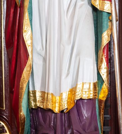 Zdjęcie nr 29: Ołtarz architektoniczny, trójosiowy, jednokondygnacyjny ze zwieńczeniem, na cokole. Mensa prostopadłościenna, drewniana, z portatylem. Antepedium na profilowanej podstawie podzielone na trzy bliskie kwadratom płyciny. Metalowe tabernakulum w formie prostopadłościanu ujętego wolutami z liści. Na ścianie frontowej drzwiczki dekorowane hostią z literami IHS ujętą od dołu rozłożonymi dłońmi.  Osie nastawy wydzielone dwiema parami pilastrów i stojącymi przed licem ołtarza kolumnami z kapitelami kompozytowymi. Wewnętrzna para kolumn dźwiga imposty z przerwanym przyczółkiem, na którym siedzi para klęczących aniołów, zaś zewnętrzna para dźwiga imposty z aniołami półleżącymi. Pole środkowe tworzy szeroka, wypełniona ażurowym akantem i rozetami rama w formie stojącego prostokąta zamkniętego łukiem nadwieszonym, ujęta lizenami, podtrzymywana przez konsole, z obrazem św. Wawrzyńca wymiennie z obrazem św. Józefa oraz rzeźbionym krucyfiksem. W osiach bocznych figury św. Stanisława po lewej i św. Wojciecha po prawej stronie, na tle arkad z ażurową kratką. Zwieńczenie tworzy grupa rzeźbiarska z przedstawieniem Trójcy Świętej. Bóg Ojciec i Chrystus siedzą zwróceni do siebie, na tle ulistionych wolut, które podtrzymują gołębicę Ducha Świetego, nad którą unosi się Oko Opatrzności. Grupa jest flankowana przez jońskie kolumny ze zwróconymi na zewnątrz wolutami, ujęta fragmentami wici tworzącymi spływy wolutowe. Cokoły kolumn dekorowane płycinami z akantem, rozetą i liliami heraldycznymi, zwieńczone ząbkowaniem. W przyłuczach dekoracja roślinna. Płycinę lizen zdobią festony z wstęgą regencyjną. Trzony pilastrów podzielone na dwie płyciny o wklęsłych bokach, dekorowane rozetami. Architrawy i fryzy dekorowane rozetami z akantu, gzyms z ząbkowaniem. Kolumny zwieńczenia dekorowane akantowymi spływami wolutowymi. Ołtarz polichromowany na ciemnoczerwono; ornamentyka oraz detale architektoniczne złocone i srebrzone. 