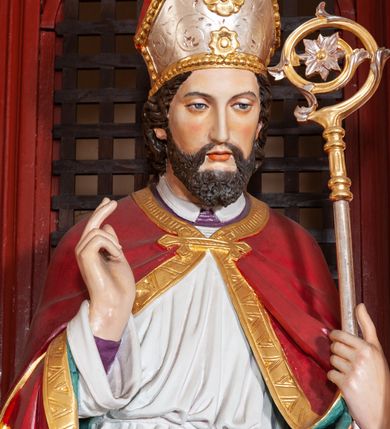 Zdjęcie nr 32: Ołtarz architektoniczny, trójosiowy, jednokondygnacyjny ze zwieńczeniem, na cokole. Mensa prostopadłościenna, drewniana, z portatylem. Antepedium na profilowanej podstawie podzielone na trzy bliskie kwadratom płyciny. Metalowe tabernakulum w formie prostopadłościanu ujętego wolutami z liści. Na ścianie frontowej drzwiczki dekorowane hostią z literami IHS ujętą od dołu rozłożonymi dłońmi.  Osie nastawy wydzielone dwiema parami pilastrów i stojącymi przed licem ołtarza kolumnami z kapitelami kompozytowymi. Wewnętrzna para kolumn dźwiga imposty z przerwanym przyczółkiem, na którym siedzi para klęczących aniołów, zaś zewnętrzna para dźwiga imposty z aniołami półleżącymi. Pole środkowe tworzy szeroka, wypełniona ażurowym akantem i rozetami rama w formie stojącego prostokąta zamkniętego łukiem nadwieszonym, ujęta lizenami, podtrzymywana przez konsole, z obrazem św. Wawrzyńca wymiennie z obrazem św. Józefa oraz rzeźbionym krucyfiksem. W osiach bocznych figury św. Stanisława po lewej i św. Wojciecha po prawej stronie, na tle arkad z ażurową kratką. Zwieńczenie tworzy grupa rzeźbiarska z przedstawieniem Trójcy Świętej. Bóg Ojciec i Chrystus siedzą zwróceni do siebie, na tle ulistionych wolut, które podtrzymują gołębicę Ducha Świetego, nad którą unosi się Oko Opatrzności. Grupa jest flankowana przez jońskie kolumny ze zwróconymi na zewnątrz wolutami, ujęta fragmentami wici tworzącymi spływy wolutowe. Cokoły kolumn dekorowane płycinami z akantem, rozetą i liliami heraldycznymi, zwieńczone ząbkowaniem. W przyłuczach dekoracja roślinna. Płycinę lizen zdobią festony z wstęgą regencyjną. Trzony pilastrów podzielone na dwie płyciny o wklęsłych bokach, dekorowane rozetami. Architrawy i fryzy dekorowane rozetami z akantu, gzyms z ząbkowaniem. Kolumny zwieńczenia dekorowane akantowymi spływami wolutowymi. Ołtarz polichromowany na ciemnoczerwono; ornamentyka oraz detale architektoniczne złocone i srebrzone. 