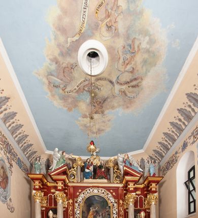 Zdjęcie nr 41: Ołtarz architektoniczny, trójosiowy, jednokondygnacyjny ze zwieńczeniem, na cokole. Mensa prostopadłościenna, drewniana, z portatylem. Antepedium na profilowanej podstawie podzielone na trzy bliskie kwadratom płyciny. Metalowe tabernakulum w formie prostopadłościanu ujętego wolutami z liści. Na ścianie frontowej drzwiczki dekorowane hostią z literami IHS ujętą od dołu rozłożonymi dłońmi.  Osie nastawy wydzielone dwiema parami pilastrów i stojącymi przed licem ołtarza kolumnami z kapitelami kompozytowymi. Wewnętrzna para kolumn dźwiga imposty z przerwanym przyczółkiem, na którym siedzi para klęczących aniołów, zaś zewnętrzna para dźwiga imposty z aniołami półleżącymi. Pole środkowe tworzy szeroka, wypełniona ażurowym akantem i rozetami rama w formie stojącego prostokąta zamkniętego łukiem nadwieszonym, ujęta lizenami, podtrzymywana przez konsole, z obrazem św. Wawrzyńca wymiennie z obrazem św. Józefa oraz rzeźbionym krucyfiksem. W osiach bocznych figury św. Stanisława po lewej i św. Wojciecha po prawej stronie, na tle arkad z ażurową kratką. Zwieńczenie tworzy grupa rzeźbiarska z przedstawieniem Trójcy Świętej. Bóg Ojciec i Chrystus siedzą zwróceni do siebie, na tle ulistionych wolut, które podtrzymują gołębicę Ducha Świetego, nad którą unosi się Oko Opatrzności. Grupa jest flankowana przez jońskie kolumny ze zwróconymi na zewnątrz wolutami, ujęta fragmentami wici tworzącymi spływy wolutowe. Cokoły kolumn dekorowane płycinami z akantem, rozetą i liliami heraldycznymi, zwieńczone ząbkowaniem. W przyłuczach dekoracja roślinna. Płycinę lizen zdobią festony z wstęgą regencyjną. Trzony pilastrów podzielone na dwie płyciny o wklęsłych bokach, dekorowane rozetami. Architrawy i fryzy dekorowane rozetami z akantu, gzyms z ząbkowaniem. Kolumny zwieńczenia dekorowane akantowymi spływami wolutowymi. Ołtarz polichromowany na ciemnoczerwono; ornamentyka oraz detale architektoniczne złocone i srebrzone. 