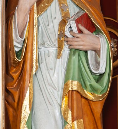 Zdjęcie nr 2: Figura drążona, na cokole. Święty Wojciech został ukazany w pozycji stojącej z uniesionymi rękami, w prawej trzyma podwójny krzyż misyjny, w lewej zaś, przy piersi, oprawioną w czerwień księgę z zaznaczonym palcem fragmentem. Twarz ma pociągłą, brwi wąskie, oczy szeroko otwarte, nos prosty, wąski i długą, sięgającą dekoltu brodę. Postać jest ubrana w fioletową albę, białą komżę ze złoconą bordiurą i ściśle przylegającą do ciała pomarańczową kapę, podbitą zielenią. Na nią ma załozony złoty paliusz, na głowie infułę, na nogach ciemnobrązowe buty. Draperia delikatnie fałdowana, odzwierciedla układ ciała. W partiach ciała polichromia naturalistyczna.