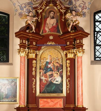 Zdjęcie nr 1: Ołtarz przyścienny, architektoniczny, jednoosiowy, jednokondygnacjowy ze zwieńczeniem. Mensa prostopadłościenna, antepedium ujęte ramą, z monogramem maryjnym na środku. Retabulum ustawione na wysokim cokole, przed którym stoi prostopadłościenna mensa. Główne pole retabulum flankują kolumny ustawione na tle filarów. Podpory mają głowice kompozytowe i są posadowione na ukośnie ustawionych, rozsuniętych postumentach dekorowanych płycinami. Dźwigają  odcinki belkowania także ustawione skośnie. W prostokątnym polu głównym nastawy ołtarzowej obraz z przedstawieniem Matki Boskiej z Dzieciątkiem, wymiennie z płótnem przedstawiającym Najświętsze Serce Jezusa i św. Stanisława Kostkę w prostokątnej ramie zamkniętej od góry łukiem półokrągłym. Na fryzie belkowania umieszczono rozety. Na zewnętrznych odcinkach belkowania, na osi kolumn, skierowane do wewnątrz woluty; na nich siedzą anioły prezentujące obraz zwieńczenia. Zwieńczenie w formie wklęsło-wypukłej, wypełnione wizerunkiem Ecce Homo we wklęsło-wypukłej ramie z łukiem nadwieszonym, jest zamknięte od góry dwiema wolutami. W miejscu ich styku, na osi palmeta. Struktura ołtarza polichromowana na brązowo; kolumny i płyciny z imitacją marmoryzacji, jasnoczerwone;  profile,  detale i ornamenty złocone. 