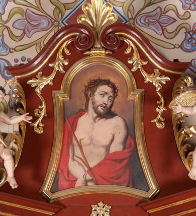 Zdjęcie nr 11: Ołtarz przyścienny, architektoniczny, jednoosiowy, jednokondygnacjowy ze zwieńczeniem. Mensa prostopadłościenna, antepedium ujęte ramą, z monogramem maryjnym na środku. Retabulum ustawione na wysokim cokole, przed którym stoi prostopadłościenna mensa. Główne pole retabulum flankują kolumny ustawione na tle filarów. Podpory mają głowice kompozytowe i są posadowione na ukośnie ustawionych, rozsuniętych postumentach dekorowanych płycinami. Dźwigają  odcinki belkowania także ustawione skośnie. W prostokątnym polu głównym nastawy ołtarzowej obraz z przedstawieniem Matki Boskiej z Dzieciątkiem, wymiennie z płótnem przedstawiającym Najświętsze Serce Jezusa i św. Stanisława Kostkę w prostokątnej ramie zamkniętej od góry łukiem półokrągłym. Na fryzie belkowania umieszczono rozety. Na zewnętrznych odcinkach belkowania, na osi kolumn, skierowane do wewnątrz woluty; na nich siedzą anioły prezentujące obraz zwieńczenia. Zwieńczenie w formie wklęsło-wypukłej, wypełnione wizerunkiem Ecce Homo we wklęsło-wypukłej ramie z łukiem nadwieszonym, jest zamknięte od góry dwiema wolutami. W miejscu ich styku, na osi palmeta. Struktura ołtarza polichromowana na brązowo; kolumny i płyciny z imitacją marmoryzacji, jasnoczerwone;  profile,  detale i ornamenty złocone. 