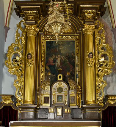 Zdjęcie nr 1: Ołtarz drewniany, architektoniczny, jednoosiowy, jednokondygnacyjny, ze zwieńczeniem, z dwiema bramkami. Jest umieszczony na murowanym, dwustopniowym podwyższeniu. Podstawa ołtarza murowana, skrzyniowa o kształcie prostopadłościanu, o obudowie drewnianej. Brak kamiennej mensy ołtarzowej. W partii antepedium nisza w kształcie prostokąta leżącego. Na mensie ustawione tabernakulum w formie centralnego kościółka zwieńczonego kopułą z latarnią.

Retabulum jest flankowane dwiema złoconymi kolumnami kompozytowymi, ustawionymi na profilowanych cokołach. Trzony kolumn są kanelowane, ozdobione w połowie wysokości główkami aniołków ujętymi dekoracją chrząstkową. Kolumny dźwigają belkowanie z wydatnym, przełamującym się nad nimi gzymsem, ozdobione ornamentem małżowinowym. W polu środkowym ołtarza profilowana, złocona i malowana rama z górną krawędzią w formie arkady z kluczem, dolna krawędź zaakcentowana uskokiem. W niej druga rama, prostokątna, ozdobiona ornamentem małżowinowym i złocona, z obrazem przedstawiającym Św. Annę Samotrzeć w otoczeniu świętych. We wnęce, za zasuwą, widnieje obraz Matki Boskiej z Dzieciątkiem w prostokątnej ramie, rzeźbionej i złoconej, pokrytej ornamentem roślinnym. Wnęka pokryta ciemnoczerwonym aksamitem, poniżej obrazu zawieszone wota. W polu arkady, w półkolistym tympanonie, na tle złoconych obłoków srebrna gołębica Ducha Świętego. Na gzymsie, na osi kolumn wazony z kwiatami. Po bokach retabulum bogato rzeźbione i złocone uszy z bujnym ornamentem małżowinowym. W zwieńczeniu, w owalnej, profilowanej i złoconej ramie obraz przedstawiający Wniebowzięcie Najświętszej Marii Panny. Rama otoczona szeroko rozbudowaną ornamentyką małżowinową. Po bokach ołtarza bramki prowadzące za ołtarz, o kształcie prostokąta stojącego, ze zwieńczeniem w formie łuku kotarowego zamkniętego od góry prostym odcinkiem, z profilowanym cokołem (pod figurę) z podwieszonym ornamentem w kształcie muszli. Górne narożniki bramek podkreślone złoconym ornamentem w kształcie wolut z elementem roślinnym. Otwór wejściowy, w kształcie analogicznym do bramki, z profilowanymi krawędziami, zakryty kotarą z aksamitu w kolorze ciemnoczerwonym. Struktura ołtarza polichromowana w kolorze ciemnobrązowym. Kolumny, pilastry, profilowania i dekoracja rzeźbiarska złocone.
