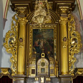Zdjęcie nr 1: Ołtarz drewniany, architektoniczny, jednoosiowy, jednokondygnacyjny, ze zwieńczeniem, z dwiema bramkami. Jest umieszczony na murowanym, dwustopniowym podwyższeniu. Podstawa ołtarza murowana, skrzyniowa o kształcie prostopadłościanu, o obudowie drewnianej. Brak kamiennej mensy ołtarzowej. W partii antepedium nisza w kształcie prostokąta leżącego. Na mensie ustawione tabernakulum w formie centralnego kościółka zwieńczonego kopułą z latarnią.

Retabulum jest flankowane dwiema złoconymi kolumnami kompozytowymi, ustawionymi na profilowanych cokołach. Trzony kolumn są kanelowane, ozdobione w połowie wysokości główkami aniołków ujętymi dekoracją chrząstkową. Kolumny dźwigają belkowanie z wydatnym, przełamującym się nad nimi gzymsem, ozdobione ornamentem małżowinowym. W polu środkowym ołtarza profilowana, złocona i malowana rama z górną krawędzią w formie arkady z kluczem, dolna krawędź zaakcentowana uskokiem. W niej druga rama, prostokątna, ozdobiona ornamentem małżowinowym i złocona, z obrazem przedstawiającym Św. Annę Samotrzeć w otoczeniu świętych. We wnęce, za zasuwą, widnieje obraz Matki Boskiej z Dzieciątkiem w prostokątnej ramie, rzeźbionej i złoconej, pokrytej ornamentem roślinnym. Wnęka pokryta ciemnoczerwonym aksamitem, poniżej obrazu zawieszone wota. W polu arkady, w półkolistym tympanonie, na tle złoconych obłoków srebrna gołębica Ducha Świętego. Na gzymsie, na osi kolumn wazony z kwiatami. Po bokach retabulum bogato rzeźbione i złocone uszy z bujnym ornamentem małżowinowym. W zwieńczeniu, w owalnej, profilowanej i złoconej ramie obraz przedstawiający Wniebowzięcie Najświętszej Marii Panny. Rama otoczona szeroko rozbudowaną ornamentyką małżowinową. Po bokach ołtarza bramki prowadzące za ołtarz, o kształcie prostokąta stojącego, ze zwieńczeniem w formie łuku kotarowego zamkniętego od góry prostym odcinkiem, z profilowanym cokołem (pod figurę) z podwieszonym ornamentem w kształcie muszli. Górne narożniki bramek podkreślone złoconym ornamentem w kształcie wolut z elementem roślinnym. Otwór wejściowy, w kształcie analogicznym do bramki, z profilowanymi krawędziami, zakryty kotarą z aksamitu w kolorze ciemnoczerwonym. Struktura ołtarza polichromowana w kolorze ciemnobrązowym. Kolumny, pilastry, profilowania i dekoracja rzeźbiarska złocone.