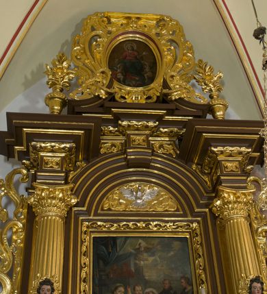 Zdjęcie nr 32: Ołtarz drewniany, architektoniczny, jednoosiowy, jednokondygnacyjny, ze zwieńczeniem, z dwiema bramkami. Jest umieszczony na murowanym, dwustopniowym podwyższeniu. Podstawa ołtarza murowana, skrzyniowa o kształcie prostopadłościanu, o obudowie drewnianej. Brak kamiennej mensy ołtarzowej. W partii antepedium nisza w kształcie prostokąta leżącego. Na mensie ustawione tabernakulum w formie centralnego kościółka zwieńczonego kopułą z latarnią.

Retabulum jest flankowane dwiema złoconymi kolumnami kompozytowymi, ustawionymi na profilowanych cokołach. Trzony kolumn są kanelowane, ozdobione w połowie wysokości główkami aniołków ujętymi dekoracją chrząstkową. Kolumny dźwigają belkowanie z wydatnym, przełamującym się nad nimi gzymsem, ozdobione ornamentem małżowinowym. W polu środkowym ołtarza profilowana, złocona i malowana rama z górną krawędzią w formie arkady z kluczem, dolna krawędź zaakcentowana uskokiem. W niej druga rama, prostokątna, ozdobiona ornamentem małżowinowym i złocona, z obrazem przedstawiającym Św. Annę Samotrzeć w otoczeniu świętych. We wnęce, za zasuwą, widnieje obraz Matki Boskiej z Dzieciątkiem w prostokątnej ramie, rzeźbionej i złoconej, pokrytej ornamentem roślinnym. Wnęka pokryta ciemnoczerwonym aksamitem, poniżej obrazu zawieszone wota. W polu arkady, w półkolistym tympanonie, na tle złoconych obłoków srebrna gołębica Ducha Świętego. Na gzymsie, na osi kolumn wazony z kwiatami. Po bokach retabulum bogato rzeźbione i złocone uszy z bujnym ornamentem małżowinowym. W zwieńczeniu, w owalnej, profilowanej i złoconej ramie obraz przedstawiający Wniebowzięcie Najświętszej Marii Panny. Rama otoczona szeroko rozbudowaną ornamentyką małżowinową. Po bokach ołtarza bramki prowadzące za ołtarz, o kształcie prostokąta stojącego, ze zwieńczeniem w formie łuku kotarowego zamkniętego od góry prostym odcinkiem, z profilowanym cokołem (pod figurę) z podwieszonym ornamentem w kształcie muszli. Górne narożniki bramek podkreślone złoconym ornamentem w kształcie wolut z elementem roślinnym. Otwór wejściowy, w kształcie analogicznym do bramki, z profilowanymi krawędziami, zakryty kotarą z aksamitu w kolorze ciemnoczerwonym. Struktura ołtarza polichromowana w kolorze ciemnobrązowym. Kolumny, pilastry, profilowania i dekoracja rzeźbiarska złocone.