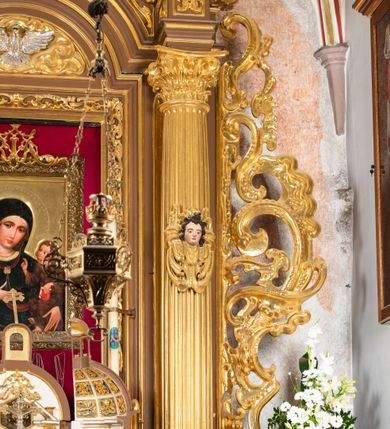 Zdjęcie nr 23: Ołtarz drewniany, architektoniczny, jednoosiowy, jednokondygnacyjny, ze zwieńczeniem, z dwiema bramkami. Jest umieszczony na murowanym, dwustopniowym podwyższeniu. Podstawa ołtarza murowana, skrzyniowa o kształcie prostopadłościanu, o obudowie drewnianej. Brak kamiennej mensy ołtarzowej. W partii antepedium nisza w kształcie prostokąta leżącego. Na mensie ustawione tabernakulum w formie centralnego kościółka zwieńczonego kopułą z latarnią.

Retabulum jest flankowane dwiema złoconymi kolumnami kompozytowymi, ustawionymi na profilowanych cokołach. Trzony kolumn są kanelowane, ozdobione w połowie wysokości główkami aniołków ujętymi dekoracją chrząstkową. Kolumny dźwigają belkowanie z wydatnym, przełamującym się nad nimi gzymsem, ozdobione ornamentem małżowinowym. W polu środkowym ołtarza profilowana, złocona i malowana rama z górną krawędzią w formie arkady z kluczem, dolna krawędź zaakcentowana uskokiem. W niej druga rama, prostokątna, ozdobiona ornamentem małżowinowym i złocona, z obrazem przedstawiającym Św. Annę Samotrzeć w otoczeniu świętych. We wnęce, za zasuwą, widnieje obraz Matki Boskiej z Dzieciątkiem w prostokątnej ramie, rzeźbionej i złoconej, pokrytej ornamentem roślinnym. Wnęka pokryta ciemnoczerwonym aksamitem, poniżej obrazu zawieszone wota. W polu arkady, w półkolistym tympanonie, na tle złoconych obłoków srebrna gołębica Ducha Świętego. Na gzymsie, na osi kolumn wazony z kwiatami. Po bokach retabulum bogato rzeźbione i złocone uszy z bujnym ornamentem małżowinowym. W zwieńczeniu, w owalnej, profilowanej i złoconej ramie obraz przedstawiający Wniebowzięcie Najświętszej Marii Panny. Rama otoczona szeroko rozbudowaną ornamentyką małżowinową. Po bokach ołtarza bramki prowadzące za ołtarz, o kształcie prostokąta stojącego, ze zwieńczeniem w formie łuku kotarowego zamkniętego od góry prostym odcinkiem, z profilowanym cokołem (pod figurę) z podwieszonym ornamentem w kształcie muszli. Górne narożniki bramek podkreślone złoconym ornamentem w kształcie wolut z elementem roślinnym. Otwór wejściowy, w kształcie analogicznym do bramki, z profilowanymi krawędziami, zakryty kotarą z aksamitu w kolorze ciemnoczerwonym. Struktura ołtarza polichromowana w kolorze ciemnobrązowym. Kolumny, pilastry, profilowania i dekoracja rzeźbiarska złocone.