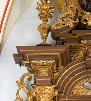 Zdjęcie nr 21: Ołtarz drewniany, architektoniczny, jednoosiowy, jednokondygnacyjny, ze zwieńczeniem, z dwiema bramkami. Jest umieszczony na murowanym, dwustopniowym podwyższeniu. Podstawa ołtarza murowana, skrzyniowa o kształcie prostopadłościanu, o obudowie drewnianej. Brak kamiennej mensy ołtarzowej. W partii antepedium nisza w kształcie prostokąta leżącego. Na mensie ustawione tabernakulum w formie centralnego kościółka zwieńczonego kopułą z latarnią.

Retabulum jest flankowane dwiema złoconymi kolumnami kompozytowymi, ustawionymi na profilowanych cokołach. Trzony kolumn są kanelowane, ozdobione w połowie wysokości główkami aniołków ujętymi dekoracją chrząstkową. Kolumny dźwigają belkowanie z wydatnym, przełamującym się nad nimi gzymsem, ozdobione ornamentem małżowinowym. W polu środkowym ołtarza profilowana, złocona i malowana rama z górną krawędzią w formie arkady z kluczem, dolna krawędź zaakcentowana uskokiem. W niej druga rama, prostokątna, ozdobiona ornamentem małżowinowym i złocona, z obrazem przedstawiającym Św. Annę Samotrzeć w otoczeniu świętych. We wnęce, za zasuwą, widnieje obraz Matki Boskiej z Dzieciątkiem w prostokątnej ramie, rzeźbionej i złoconej, pokrytej ornamentem roślinnym. Wnęka pokryta ciemnoczerwonym aksamitem, poniżej obrazu zawieszone wota. W polu arkady, w półkolistym tympanonie, na tle złoconych obłoków srebrna gołębica Ducha Świętego. Na gzymsie, na osi kolumn wazony z kwiatami. Po bokach retabulum bogato rzeźbione i złocone uszy z bujnym ornamentem małżowinowym. W zwieńczeniu, w owalnej, profilowanej i złoconej ramie obraz przedstawiający Wniebowzięcie Najświętszej Marii Panny. Rama otoczona szeroko rozbudowaną ornamentyką małżowinową. Po bokach ołtarza bramki prowadzące za ołtarz, o kształcie prostokąta stojącego, ze zwieńczeniem w formie łuku kotarowego zamkniętego od góry prostym odcinkiem, z profilowanym cokołem (pod figurę) z podwieszonym ornamentem w kształcie muszli. Górne narożniki bramek podkreślone złoconym ornamentem w kształcie wolut z elementem roślinnym. Otwór wejściowy, w kształcie analogicznym do bramki, z profilowanymi krawędziami, zakryty kotarą z aksamitu w kolorze ciemnoczerwonym. Struktura ołtarza polichromowana w kolorze ciemnobrązowym. Kolumny, pilastry, profilowania i dekoracja rzeźbiarska złocone.