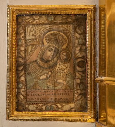 Zdjęcie nr 39: Ołtarz drewniany, architektoniczny, jednoosiowy, jednokondygnacyjny, ze zwieńczeniem, z dwiema bramkami. Jest umieszczony na murowanym, dwustopniowym podwyższeniu. Podstawa ołtarza murowana, skrzyniowa o kształcie prostopadłościanu, o obudowie drewnianej. Brak kamiennej mensy ołtarzowej. W partii antepedium nisza w kształcie prostokąta leżącego. Na mensie ustawione tabernakulum w formie centralnego kościółka zwieńczonego kopułą z latarnią.

Retabulum jest flankowane dwiema złoconymi kolumnami kompozytowymi, ustawionymi na profilowanych cokołach. Trzony kolumn są kanelowane, ozdobione w połowie wysokości główkami aniołków ujętymi dekoracją chrząstkową. Kolumny dźwigają belkowanie z wydatnym, przełamującym się nad nimi gzymsem, ozdobione ornamentem małżowinowym. W polu środkowym ołtarza profilowana, złocona i malowana rama z górną krawędzią w formie arkady z kluczem, dolna krawędź zaakcentowana uskokiem. W niej druga rama, prostokątna, ozdobiona ornamentem małżowinowym i złocona, z obrazem przedstawiającym Św. Annę Samotrzeć w otoczeniu świętych. We wnęce, za zasuwą, widnieje obraz Matki Boskiej z Dzieciątkiem w prostokątnej ramie, rzeźbionej i złoconej, pokrytej ornamentem roślinnym. Wnęka pokryta ciemnoczerwonym aksamitem, poniżej obrazu zawieszone wota. W polu arkady, w półkolistym tympanonie, na tle złoconych obłoków srebrna gołębica Ducha Świętego. Na gzymsie, na osi kolumn wazony z kwiatami. Po bokach retabulum bogato rzeźbione i złocone uszy z bujnym ornamentem małżowinowym. W zwieńczeniu, w owalnej, profilowanej i złoconej ramie obraz przedstawiający Wniebowzięcie Najświętszej Marii Panny. Rama otoczona szeroko rozbudowaną ornamentyką małżowinową. Po bokach ołtarza bramki prowadzące za ołtarz, o kształcie prostokąta stojącego, ze zwieńczeniem w formie łuku kotarowego zamkniętego od góry prostym odcinkiem, z profilowanym cokołem (pod figurę) z podwieszonym ornamentem w kształcie muszli. Górne narożniki bramek podkreślone złoconym ornamentem w kształcie wolut z elementem roślinnym. Otwór wejściowy, w kształcie analogicznym do bramki, z profilowanymi krawędziami, zakryty kotarą z aksamitu w kolorze ciemnoczerwonym. Struktura ołtarza polichromowana w kolorze ciemnobrązowym. Kolumny, pilastry, profilowania i dekoracja rzeźbiarska złocone.