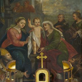 Zdjęcie nr 1: Obraz w kształcie stojącego prostokąta, w ramie rzeźbionej, malowanej, złoconej i ozdobionej ornamentem małżowinowym. Ukazuje św. Annę, Marię i Jezusa oraz świętych Wojciecha, Stanisława, Katarzynę i Tomasza. Na dwudzielnej ławie umieszczonej na podwyższeniu siedzi: po lewej stronie Najświętsza Maria Panna, po prawej św. Anna. Obie niewiasty zwrócone są ku stojącemu pomiędzy nimi Dzieciątku. Nagi Chrystus, okryty na skos białą chustą, przytrzymywaną na Jego prawym boku przez obie niewiasty, ukazany frontalnie, z wysuniętą ku przodowi prawą nóżką i lewą podtrzymywaną przez św. Annę. Prawą rękę wznosi w geście błogosławieństwa, zaś lewa obejmuje św. Annę. Głowę Chrystusa, ozdobioną jasno złotobrązowymi włosami, otacza promienista gloria. 
Najświętsza Maria Panna, lekko pochylona w kierunku Chrystusa, ubrana jest w czerwoną suknię i niebieski płaszcz założony na lewe ramię. Jej głowa jest nakryta jasnozieloną chustą, związaną z tyłu głowy, spod której wyłaniają się jasnobrązowe włosy. Twarz Marii zwrócona jest ku widzowi, ze wzrokiem skierowanym na wprost. Święta Anna w zielonej sukni i ciemnoczerwonym płaszczu, narzuconym na prawe ramię mocno pochyla się ku Chrystusowi. Głowę świętej przykrywa biała chusta ze złotymi przeszyciami, opadająca na plecy i prawe ramię. Spod chusty widoczne siwe włosy. Twarz św. Anny ukazana jest półprofilu, ze wzrokiem skierowanym ku Marii. Nad głowami Marii i św. Anny unoszą się nimby. Na pierwszym planie, u stóp niewiast klęczą zwróceni ku Jezusowi: po lewej stronie św. Wojciech w stroju biskupim, z paliuszem i z leżącym przed nim na ziemi pastorałem z podwójnym krzyżem, po prawej św. Stanisław, w stroju biskupim, z pastorałem w lewej ręce i postacią Piotrowina wyłaniającą się z grobu. W tle po prawej stronie św. Katarzyna, trzymająca miecz we wspartej na kole prawej dłoni i palmę męczeństwa w lewej, ubrana w zielona suknię i szary płaszcz. Obok niej stoi św. Tomasz, z prawą dłonią złożoną na piersi, z lilią w lewej ręce, ubrany w czarny habit. Za postaciami świętych daleki górski pejzaż. Po lewej stronie obrazu, na tle architektury z podwieszonymi ciemnoniebieskimi kotarami ozdobionymi złocistymi frędzlami i chwostem, widnieją popiersia dwóch świętych starców w jasnobrązowych szatach. Głowy świętych otaczają nimby. W górnej części, na osi obrazu popiersie Boga Ojca z trójkątnym nimbem, poniżej gołębica Ducha Świętego, otoczona promienistą glorią. Kolorystyka obrazu stonowana, ciepła, nasycona. Kolorystyczną dominantę stanowi ciemny błękit płaszcza Marii, czerwień płaszcza i zieleń sukni św. Anny. Kolory te podkreślają jasną postać Chrystusa.