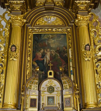 Zdjęcie nr 2: Obraz w kształcie stojącego prostokąta, w ramie rzeźbionej, malowanej, złoconej i ozdobionej ornamentem małżowinowym. Ukazuje św. Annę, Marię i Jezusa oraz świętych Wojciecha, Stanisława, Katarzynę i Tomasza. Na dwudzielnej ławie umieszczonej na podwyższeniu siedzi: po lewej stronie Najświętsza Maria Panna, po prawej św. Anna. Obie niewiasty zwrócone są ku stojącemu pomiędzy nimi Dzieciątku. Nagi Chrystus, okryty na skos białą chustą, przytrzymywaną na Jego prawym boku przez obie niewiasty, ukazany frontalnie, z wysuniętą ku przodowi prawą nóżką i lewą podtrzymywaną przez św. Annę. Prawą rękę wznosi w geście błogosławieństwa, zaś lewa obejmuje św. Annę. Głowę Chrystusa, ozdobioną jasno złotobrązowymi włosami, otacza promienista gloria. 
Najświętsza Maria Panna, lekko pochylona w kierunku Chrystusa, ubrana jest w czerwoną suknię i niebieski płaszcz założony na lewe ramię. Jej głowa jest nakryta jasnozieloną chustą, związaną z tyłu głowy, spod której wyłaniają się jasnobrązowe włosy. Twarz Marii zwrócona jest ku widzowi, ze wzrokiem skierowanym na wprost. Święta Anna w zielonej sukni i ciemnoczerwonym płaszczu, narzuconym na prawe ramię mocno pochyla się ku Chrystusowi. Głowę świętej przykrywa biała chusta ze złotymi przeszyciami, opadająca na plecy i prawe ramię. Spod chusty widoczne siwe włosy. Twarz św. Anny ukazana jest półprofilu, ze wzrokiem skierowanym ku Marii. Nad głowami Marii i św. Anny unoszą się nimby. Na pierwszym planie, u stóp niewiast klęczą zwróceni ku Jezusowi: po lewej stronie św. Wojciech w stroju biskupim, z paliuszem i z leżącym przed nim na ziemi pastorałem z podwójnym krzyżem, po prawej św. Stanisław, w stroju biskupim, z pastorałem w lewej ręce i postacią Piotrowina wyłaniającą się z grobu. W tle po prawej stronie św. Katarzyna, trzymająca miecz we wspartej na kole prawej dłoni i palmę męczeństwa w lewej, ubrana w zielona suknię i szary płaszcz. Obok niej stoi św. Tomasz, z prawą dłonią złożoną na piersi, z lilią w lewej ręce, ubrany w czarny habit. Za postaciami świętych daleki górski pejzaż. Po lewej stronie obrazu, na tle architektury z podwieszonymi ciemnoniebieskimi kotarami ozdobionymi złocistymi frędzlami i chwostem, widnieją popiersia dwóch świętych starców w jasnobrązowych szatach. Głowy świętych otaczają nimby. W górnej części, na osi obrazu popiersie Boga Ojca z trójkątnym nimbem, poniżej gołębica Ducha Świętego, otoczona promienistą glorią. Kolorystyka obrazu stonowana, ciepła, nasycona. Kolorystyczną dominantę stanowi ciemny błękit płaszcza Marii, czerwień płaszcza i zieleń sukni św. Anny. Kolory te podkreślają jasną postać Chrystusa.