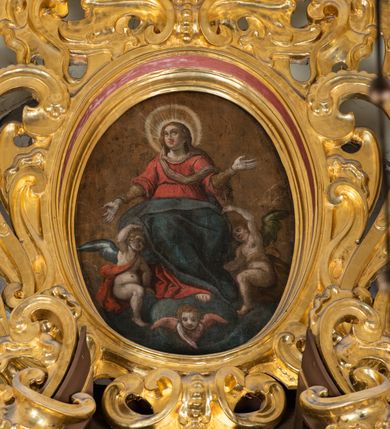 Zdjęcie nr 5: Obraz umieszczony w zwieńczeniu ołtarza głównego, w owalnej profilowanej, złoconej i malowanej ramie, ujętej ornamentem małżowinowym. W polu obrazu o kształcie owalu scena Wniebowzięcia Najświętszej Marii Panny. Dominantę kompozycji wpisanej w trójkąt stanowi ukazana frontalnie postać Marii unoszona ku niebu przez dwa nagie, antytetycznie przedstawione anioły. Pod stopami Marii i aniołów kłębią się ciemne obłoki, na ich tle, na osi kompozycji, widnieje przedstawienie cherubina. Głowa Marii nieznacznie uniesiona. Jej twarz jest okrągła, oczy duże, wzrok wzniesiony ku górze, wyraz twarzy pogodny, z delikatnym uśmiechem. Na głowie Maria ma chustę w kolorze jasnej ochry, spływającą wąską fałdą wokół szyi i przez pierś na lewe ramię, zaś wokół niej nimb składający się z promienistej glorii i złotego otoku. Ręce Marii są rozłożone, dłonie ukazane wewnętrzną stroną. Prawa ręka wyprostowana, skierowana w dół, lewa, zgięta w łokciu, skierowana ku górze. Spod sukni Marii wystaje prawa stopa z zaznaczonym konturem sandała. Madonna jest ubrana w wysoko przepasaną czerwoną suknię, z podwiniętymi szerokimi rękawami, spod których wystają wąskie długie rękawy spodniej szaty w kolorze jasnej ochry oraz ciemnoniebieski, szeroki płaszcz okrywający jej kolana. Fałdy płaszcza zaznaczone  łamiącymi się liniami.  
Obejmujące kolana Marii i zwrócone ku niej anioły są nagie, przepasane jedynie szarfami: anioł z ciemnoniebieskim skrzydłem, po prawej stronie Matki Boskiej – szarfą czerwoną, przełożoną przez lewe ramię do prawego boku i związaną wydatnym węzłem, anioł z ciemnozielonym skrzydłem, po lewej stronie Marii – szarfą w kolorze jasnej ochry, przewiązaną w pasie, w węzłem na plecach. 
Tło monochromatyczne, w odcieniach jasnego brązu i ochry. Kontury postaci podkreślone ciemnym brązem i czernią. Karnacje twarzy naturalne, modelowane światłocieniowo, policzki podkreślone różem. Włosy Marii i aniołów w kolorze jasnego brązu. Skrzydła aniołów i cherubina modelowane bielą. Kolorystyka obrazu stonowana, ciepła, nasycona. Dominantę kolorystyczną stanowi czerwień i ciemny błękit szat Najświętszej Marii Panny.