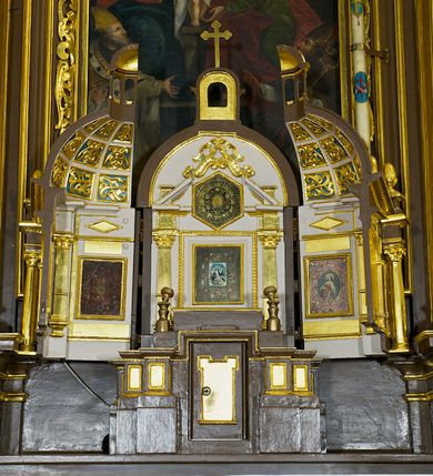 Zdjęcie nr 2: Tabernakulum w formie centralnego kościoła z kopułą. Całość na wysokim profilowanym cokole, flankującym właściwe Sakramentarium, z drzwiczkami w kształcie stojącego prostokąta, ozdobionymi płyciną z uszakami w górnych narożnikach, ujętymi od góry nadwieszonym prostokątnym profilowanym obramieniem. Na cokole cztery pary kolumn korynckich ustawionych uskokowo, flankujących centralną arkadę zakończoną łukiem półkolistym. Kolumny dźwigają belkowanie z wydatnym przełamującym się gzymsem, zwieńczone trójkątnym profilowanym przyczółkiem. Ponad kolumnami, ustawione na profilowanych impostach dekoracyjne szyszki. Kopuła z pionowymi podziałami, ozdobionymi ornamentem małżowinowym, zwieńczona latarnią z przeźroczami w postaci półkolistych arkad i kopułką. Całość zwieńczona krzyżem o ramionach zakończonych trójliściem. 
Górna część tabernakulum wraz z kopułą otwierana drzwiczkami dwuskrzydłowymi, łamanymi, dwuelementowymi. Wewnątrz na ścianach podziały architektoniczne zaznaczone korynckimi pilastrami wspierającymi belkowanie, ustawionymi na wysokich cokołach. W części środkowej pilastry dźwigają belkowanie z przełamującym się gzymsem i zwieńczeniem trójkątnym przerwanym, ozdobionym motywem złożonym z ornamentu małżowinowego. W polu tympanonu i belkowania rozeta inkrustowana bursztynem, ujęta ramą w kształcie sześcioboku. Na ścianach wewnętrznych obrazki relikwiarzowe, w profilowanych ramach, oszklone. W środkowym przedstawienie św. Katarzyny Sieneńskiej z aniołami, nad nim owalne pole wpisane w oktagon z owalną kasztą obwiedzione kwiatami i glorią promienistą, w kwiatach wydrukowane słowa: &quot;AGNUS OMBRA DE [...]&quot;. Na dwóch lewych ściankach tkany wizerunek Matki Boskiej Krakowskiej z podpisem: &quot; IMAGO M. MIRACVLOSA B(EATAE) V(IRGINIS) M(ARIAE) / IN ECCLESIA CARMELITA/NVM CRACOVIE IN ARENIS&quot; oraz relikwie w owalnej kaszcie obwiedzionej abstrakcyjnym, symetrycznym wzorem wykonanym z metalowych blaszek. Na ściankach z prawej strony owalne przedstawienie św. Katarzyny Aleksandryjskiej otoczone stylizowanymi wiciami z blaszek i relikwiami wielu świętych opisanych na banderolach oraz przedstawienie Ecce Homo z podpisem &quot;ECCE HOMO&quot; i monogramem imienia Jezus (u góry) i maryjsnym (u dołu). Podniebie kopuły wypełnione perspektywicznymi kasetonami ozdobionymi ornamentem małżowinowym. Struktura tabernakulum w kolorze ciemnobrązowym, pola arkady, płyciny i pola wewnętrzne jasnobeżowe, pola kasetonów niebieskie, kolumny, pilastry, profilowania i ornamenty złocone.