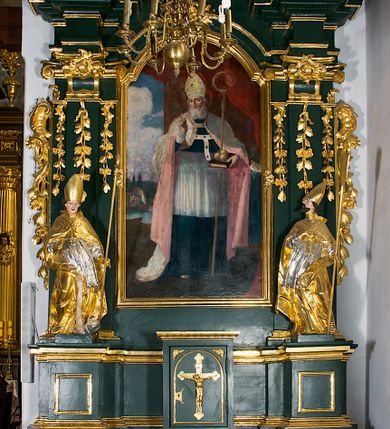 Zdjęcie nr 1: Ołtarz przyścienny, architektoniczny, jednokondygnacyjny, jednoosiowy ze zwieńczeniem. Umieszczony na dwustopniowym, kamiennym podwyższeniu. Mensa prostopadłościenna, z portatylem i współczesnym antepedium ozdobionym postacią św. Weroniki trzymającej chustę z odbiciem twarzy Chrystusa (veraikon) i rzeźbionym ornamentem ze srebrzonych liści i złoconych kiści winogron; tło w kolorze struktury ołtarza. Retabulum na wysokim profilowanym, dwustopniowym cokole, flankowane zwielokrotnionymi pilastrami z jońskimi kapitelami. Pilastry dźwigają przerwane belkowanie z wydatnym profilowanym gzymsem z przerwanym przyczółkiem. Zwieńczenie o wklęsłych bokach ujęte spływami wolutowymi dźwigającymi gzyms w formie nadwieszonego łuku odcinkowego. Na tle pilastrów ustawione na profilowanych impostach rzeźby: po prawej stronie św. Wojciecha, po lewej św. Stanisława. Na przyczółkach znajdują się siedzące putta. Pole środkowe o kształcie prostokąta stojącego od góry zamkniętego łukiem półkolistym nadwieszonym, w kluczu ornament z motywu rocaille. Wewnątrz pola ujęty profilowaną, złoconą ramą obraz z przedstawieniem św. Mikołaja z Miry. W zwieńczeniu obraz w ramie z wklęsłymi bokami i wypukłymi dolną i górną krawędzią przedstawiający św. Marię Magdalenę. Nastawę ujmują ornamentalne uszy, utworzone z motywów rocaille'owych i liściasto-kwiatowych zwisów. Na kapitele są nałożone rocaille'owe kartusze, a pod nimi podwieszone zwisające ulistnione i ukwiecone gałązki wzbogacone motywami rocaille'ów. Struktura ołtarza polichromowana w kolorze ciemnozielonym. Bazy pilastrów, kapitele, uszy, ornamenty, profilowania, obramienia płycin i ramy obrazów złocone. Rzeźby świętych złocone, srebrzone i polichromowane. Rzeźby aniołków złocone i polichromowane.

