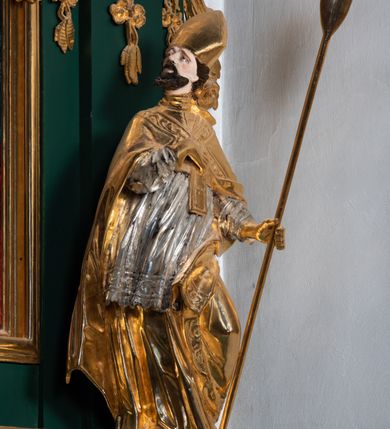 Zdjęcie nr 28: Ołtarz przyścienny, architektoniczny, jednokondygnacyjny, jednoosiowy ze zwieńczeniem. Umieszczony na dwustopniowym, kamiennym podwyższeniu. Mensa prostopadłościenna, z portatylem i współczesnym antepedium ozdobionym postacią św. Weroniki trzymającej chustę z odbiciem twarzy Chrystusa (veraikon) i rzeźbionym ornamentem ze srebrzonych liści i złoconych kiści winogron; tło w kolorze struktury ołtarza. Retabulum na wysokim profilowanym, dwustopniowym cokole, flankowane zwielokrotnionymi pilastrami z jońskimi kapitelami. Pilastry dźwigają przerwane belkowanie z wydatnym profilowanym gzymsem z przerwanym przyczółkiem. Zwieńczenie o wklęsłych bokach ujęte spływami wolutowymi dźwigającymi gzyms w formie nadwieszonego łuku odcinkowego. Na tle pilastrów ustawione na profilowanych impostach rzeźby: po prawej stronie św. Wojciecha, po lewej św. Stanisława. Na przyczółkach znajdują się siedzące putta. Pole środkowe o kształcie prostokąta stojącego od góry zamkniętego łukiem półkolistym nadwieszonym, w kluczu ornament z motywu rocaille. Wewnątrz pola ujęty profilowaną, złoconą ramą obraz z przedstawieniem św. Mikołaja z Miry. W zwieńczeniu obraz w ramie z wklęsłymi bokami i wypukłymi dolną i górną krawędzią przedstawiający św. Marię Magdalenę. Nastawę ujmują ornamentalne uszy, utworzone z motywów rocaille&#039;owych i liściasto-kwiatowych zwisów. Na kapitele są nałożone rocaille&#039;owe kartusze, a pod nimi podwieszone zwisające ulistnione i ukwiecone gałązki wzbogacone motywami rocaille&#039;ów. Struktura ołtarza polichromowana w kolorze ciemnozielonym. Bazy pilastrów, kapitele, uszy, ornamenty, profilowania, obramienia płycin i ramy obrazów złocone. Rzeźby świętych złocone, srebrzone i polichromowane. Rzeźby aniołków złocone i polichromowane.

