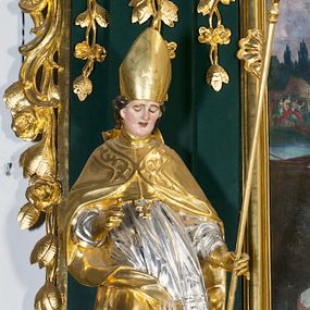 Zdjęcie nr 1: Pełnoplastyczna rzeźba drewniana przedstawiająca św. Stanisława, przyścienna, polichromowana, złocona i srebrzona, wydrążona z tyłu. Ustawiona na niskiej prostokątnej podstawie. Święty ukazany całopostaciowo, w pozycji stojącej w kontrapoście, z prawą nogą ugiętą w kolanie i odstawioną w bok, z wyraźnym przegięciem ciała w lewo i skręceniem korpusu w prawo. W lewej ręce pastorał trzymany na wysokości bioder, prawa zgięta w łokciu i uniesiona przed siebie. Głowa mała, osadzona na długiej szyi, pochylona w dół, lekko zwrócona w lewo. Twarz owalna, policzki pełne. Oczy prawie całkowicie przesłonięte powiekami, wzrok skierowany w dół. Nos duży, prosty, usta małe, pełne, o uniesionych w górę kącikach. Głowę po bokach okalają krótkie włosy układające się w wywinięte na zewnątrz pukle. Na głowie infuła ozdobiona krzyżem równoramiennym o lekko rozszerzających się ramionach, ze wstęgami na plecach. Święty ubrany w albę, rokietę z szeroką, dekoracyjną koronką i mucet. Na ramiona narzucona kapa z galonem ozdobionym stylizowanym motywem roślinnym. Na piersi widoczny pektorał, na szyi humerał, na dłoniach rękawiczki. Spod szat widoczny lewy but. Szaty świętego ukształtowane ekspresyjnie, o ostro ciętych, skośnych fałdach. Poły płaszcza wywinięte na zewnątrz. Odwinięta poła płaszcza pod prawą ręką tworzy obszerny fałd o kształcie litery "S". Z przodu figury, u stóp świętego postać wyłaniającego się z grobu Piotrowina, z mocno odchyloną do tyłu głową nakrytą całunem i wyprostowaną, wyciągniętą pionowo w górę ręką, z widocznie zaznaczonymi mięśniami i dłonią o długich, szczupłych palcach. Twarz Piotrowina wychudzona, z dużym, lekko garbatym nosem, ponad ustami proste wąsy.  Cały strój świętego, z wyjątkiem srebrzonej rokiety, złocony. Twarz i włosy polichromowane. Postać Piotrowina, z wyjątkiem srebrzonego całunu, polichromowana.