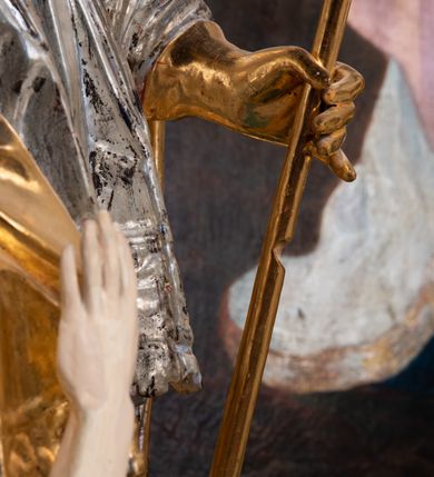 Zdjęcie nr 8: Pełnoplastyczna rzeźba drewniana przedstawiająca św. Stanisława, przyścienna, polichromowana, złocona i srebrzona, wydrążona z tyłu. Ustawiona na niskiej prostokątnej podstawie. Święty ukazany całopostaciowo, w pozycji stojącej w kontrapoście, z prawą nogą ugiętą w kolanie i odstawioną w bok, z wyraźnym przegięciem ciała w lewo i skręceniem korpusu w prawo. W lewej ręce pastorał trzymany na wysokości bioder, prawa zgięta w łokciu i uniesiona przed siebie. Głowa mała, osadzona na długiej szyi, pochylona w dół, lekko zwrócona w lewo. Twarz owalna, policzki pełne. Oczy prawie całkowicie przesłonięte powiekami, wzrok skierowany w dół. Nos duży, prosty, usta małe, pełne, o uniesionych w górę kącikach. Głowę po bokach okalają krótkie włosy układające się w wywinięte na zewnątrz pukle. Na głowie infuła ozdobiona krzyżem równoramiennym o lekko rozszerzających się ramionach, ze wstęgami na plecach. Święty ubrany w albę, rokietę z szeroką, dekoracyjną koronką i mucet. Na ramiona narzucona kapa z galonem ozdobionym stylizowanym motywem roślinnym. Na piersi widoczny pektorał, na szyi humerał, na dłoniach rękawiczki. Spod szat widoczny lewy but. Szaty świętego ukształtowane ekspresyjnie, o ostro ciętych, skośnych fałdach. Poły płaszcza wywinięte na zewnątrz. Odwinięta poła płaszcza pod prawą ręką tworzy obszerny fałd o kształcie litery &quot;S&quot;. Z przodu figury, u stóp świętego postać wyłaniającego się z grobu Piotrowina, z mocno odchyloną do tyłu głową nakrytą całunem i wyprostowaną, wyciągniętą pionowo w górę ręką, z widocznie zaznaczonymi mięśniami i dłonią o długich, szczupłych palcach. Twarz Piotrowina wychudzona, z dużym, lekko garbatym nosem, ponad ustami proste wąsy.  Cały strój świętego, z wyjątkiem srebrzonej rokiety, złocony. Twarz i włosy polichromowane. Postać Piotrowina, z wyjątkiem srebrzonego całunu, polichromowana.