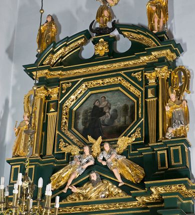 Zdjęcie nr 23: Ołtarz ustawiony na kamiennym podwyższeniu, przyścienny, architektoniczny, jednoosiowy, dwukondygnacyjny ze zwieńczeniem. Podstawa ołtarza skrzyniowa, na niej kamienna mensa z centralnie umieszczonym portatylem. Antepedium późne (secesyjne), datowane na odwrocie „1914”, ozdobione figurą anioła trzymającego wstęgę z napisem „AVE MARIA” i rzeźbionym ornamentem ze złoconych liści winogron i srebrzonych lilii. Retabulum jest flankowane dwiema parami ustawionych uskokowo i osadzonych na wysokich cokołach kolumn kompozytowych, ozdobionych główkami aniołków ujętych dekoracją małżowinową. Kolumny dźwigają belkowanie z wydatnym, przełamującym się gzymsem ozdobionym ornamentem małżowinowym. Nad belkowaniem trójkątny przyczółek z rzeźbioną figurą Boga Ojca w polu tympanonu i figurami aniołów na jego bokach. Druga kondygnacja ołtarza jest flankowana pojedynczymi kolumienkami i kanelowanymi pilasterkami korynckimi, ustawionymi na wysokich cokołach. Boki ozdobione uszami w kształcie małżowiny. Na zewnątrz kolumn, na osiach kolumn zewnętrznych niższej kondygnacji, ustawione na impostach figury: św. Kazimierza po lewej stronie, św. Stanisława po prawej. Kolumny podpierają belkowanie z przełamującym się gzymsem ozdobionym ornamentem małżowinowym, ponad którym zwieńczenie w formie przyczółka odcinkowego przerwanego. Łuk przyczółka profilowany z uskokami, dekorowany ornamentem małżowinowym. Pośrodku zwieńczenia, w przerwanym przyczółku rzeźba św. Michała Archanioła, ustawiona na wysokim cokole z dekoracją w formie bukietu granatów otoczonych liśćmi akantu. Po bokach, na osiach kolumn rzeźbione figury: św. Barbary po lewej stronie i św. Jana Chrzciciela po stronie prawej. Pomiędzy impostami kolumn, w predelli profilowana płycina w kształcie leżącego prostokąta z wyciętymi uskokowo górnymi narożnikami. W niej obraz olejny na płótnie (przyklejony do struktury) ze sceną Nawiedzenia św. Elżbiety. W polu środkowym pierwszej kondygnacji obraz z przedstawieniem Najświętszego Serca Pana Jezusa w profilowanej ramie w kształcie stojącego prostokąta, ozdobionej ornamentem małżowinowym. W drugiej kondygnacji  pole środkowe w kształcie prostokąta leżącego (zbliżonego do kwadratu), obwiedzione frezowaną ramką, z wpisaną w nią ramą o kształcie oktagonalnym, profilowaną i ozdobioną ornamentem małżowinowym, z obrazem przedstawiającym św. Antoniego. Strukturę retabulum, a także prostokątne płyciny zdobiące cokoły i tło kolumn, podkreślają frezowane ramki. Kolumny, pilastry, kapitele, ornamenty, obramienia płycin i belkowania, frezowane ramki złocone. Ramy obrazów złocone i polichromowane. Rzeźby złocone, srebrzone i polichromowane. 