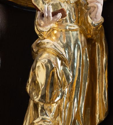 Zdjęcie nr 12: Ambona drewniana, przyścienna, wisząca, dostawiona do północnej ściany nawy ze schodkami biegnącymi wzdłuż ściany. Kosz ambony jest sześcioboczny, z niewielkim parapetem. Jego boki zostały podzielone na pola stojącymi na wysokich cokołach pięcioma kolumienkami o korynckich kapitelach, dźwigających profilowane belkowanie. W polach prostokątne płyciny z konchowymi wnękami ozdobionymi muszlami z figurami ewangelistów. 
We wnękach rzeźby z przedstawieniami ewangelistów i Chrystusa. Figury drewniane pełnoplastyczne, wydrążone od tyłu, polichromowane, złocone i srebrzone, ustawione na niewielkich prostokątnych podstawach, od lewej: św. Łukasz wsparty prawą nogą na głowie byka, św. Marek wsparty prawą nogą na głowie lwa, św. Jan z orłem przy prawej nodze, Chrystus Salvator Mundi, św. Mateusz z aniołem przy prawej nodze. Ewangeliści trzymają w prawych dłoniach otwarte księgi, z wyjątkiem św. Mateusza, trzymającego kodeks w lewej ręce. Dłonie ewangelistów nieproporcjonalnie duże. Szaty bogato pofałdowane, głęboko cięte. 
Podstawa kosza bogato profilowana, ozdobiona podwieszoną dekoracyjną szyszką. Schodki ograniczone parapetem z trzema romboidalnymi płycinami w złoconych profilowanych obramieniach. Na filarze przy wejściu na schodki złocona kula z szyszką. Zaplecek w kształcie stojącego prostokąta, w górnej części ujęty zwężającymi się ku dołowi pilastrami wypełnionymi cekinami, zwieńczonymi rombowymi wypustkami i korynckimi kapitelami, które podtrzymują przełamujące się nad nimi belkowanie. Pośrodku zaplecka w prostokątnym obramieniu zamkniętym nadwieszonym łukiem półkolistym płaskorzeźbione popiersie Boga Ojca wyłaniającego się z obłoków. Prawa ręka Boga wzniesiona w geście błogosławieństwa, lewa oparta na globie ziemskim zwieńczonym krzyżem. Tłem dla postaci Boga Ojca jest rozwiana poła płaszcza układająca się niemal półkoliście. Baldachim ośmioboczny. W profilowanym podniebiu, ozdobionym pasem ornamentu małżowinowo-chrząstkowego i profilowanymi wisiorami, gołębica Ducha Świętego na tle glorii utworzonej z prostych promieni o równej długości. Baldachim ozdobiony zamkniętą koroną, którą tworzy pięć esownic pokrytych pasami ornamentu małżowinowo-chrząstkowego. W zwieńczeniu pełnoplastyczna rzeźba przedstawiająca św. Jana Chrzciciela. Figura drewniana, wydrążona z tyłu, polichromowana, złocona i srebrzona, ustawiona na niewielkiej wielobocznej profilowanej podstawie. Święty w prawej ręce trzyma wysoki krzyż, w lewej księgę, na której spoczywa Baranek Boży. Struktura ambony ciemnobrązowa. Kolumny, kapitele, pilastry w zaplecku korona baldachimu, profilowania i ornamenty złocone, z wyjątkiem srebrzonej ramy w zaplecku i gołębicy Ducha Świętego.
