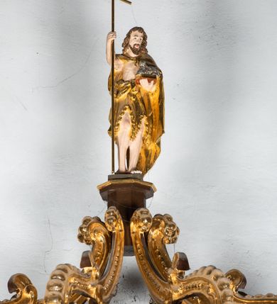 Zdjęcie nr 15: Ambona drewniana, przyścienna, wisząca, dostawiona do północnej ściany nawy ze schodkami biegnącymi wzdłuż ściany. Kosz ambony jest sześcioboczny, z niewielkim parapetem. Jego boki zostały podzielone na pola stojącymi na wysokich cokołach pięcioma kolumienkami o korynckich kapitelach, dźwigających profilowane belkowanie. W polach prostokątne płyciny z konchowymi wnękami ozdobionymi muszlami z figurami ewangelistów. 
We wnękach rzeźby z przedstawieniami ewangelistów i Chrystusa. Figury drewniane pełnoplastyczne, wydrążone od tyłu, polichromowane, złocone i srebrzone, ustawione na niewielkich prostokątnych podstawach, od lewej: św. Łukasz wsparty prawą nogą na głowie byka, św. Marek wsparty prawą nogą na głowie lwa, św. Jan z orłem przy prawej nodze, Chrystus Salvator Mundi, św. Mateusz z aniołem przy prawej nodze. Ewangeliści trzymają w prawych dłoniach otwarte księgi, z wyjątkiem św. Mateusza, trzymającego kodeks w lewej ręce. Dłonie ewangelistów nieproporcjonalnie duże. Szaty bogato pofałdowane, głęboko cięte. 
Podstawa kosza bogato profilowana, ozdobiona podwieszoną dekoracyjną szyszką. Schodki ograniczone parapetem z trzema romboidalnymi płycinami w złoconych profilowanych obramieniach. Na filarze przy wejściu na schodki złocona kula z szyszką. Zaplecek w kształcie stojącego prostokąta, w górnej części ujęty zwężającymi się ku dołowi pilastrami wypełnionymi cekinami, zwieńczonymi rombowymi wypustkami i korynckimi kapitelami, które podtrzymują przełamujące się nad nimi belkowanie. Pośrodku zaplecka w prostokątnym obramieniu zamkniętym nadwieszonym łukiem półkolistym płaskorzeźbione popiersie Boga Ojca wyłaniającego się z obłoków. Prawa ręka Boga wzniesiona w geście błogosławieństwa, lewa oparta na globie ziemskim zwieńczonym krzyżem. Tłem dla postaci Boga Ojca jest rozwiana poła płaszcza układająca się niemal półkoliście. Baldachim ośmioboczny. W profilowanym podniebiu, ozdobionym pasem ornamentu małżowinowo-chrząstkowego i profilowanymi wisiorami, gołębica Ducha Świętego na tle glorii utworzonej z prostych promieni o równej długości. Baldachim ozdobiony zamkniętą koroną, którą tworzy pięć esownic pokrytych pasami ornamentu małżowinowo-chrząstkowego. W zwieńczeniu pełnoplastyczna rzeźba przedstawiająca św. Jana Chrzciciela. Figura drewniana, wydrążona z tyłu, polichromowana, złocona i srebrzona, ustawiona na niewielkiej wielobocznej profilowanej podstawie. Święty w prawej ręce trzyma wysoki krzyż, w lewej księgę, na której spoczywa Baranek Boży. Struktura ambony ciemnobrązowa. Kolumny, kapitele, pilastry w zaplecku korona baldachimu, profilowania i ornamenty złocone, z wyjątkiem srebrzonej ramy w zaplecku i gołębicy Ducha Świętego.