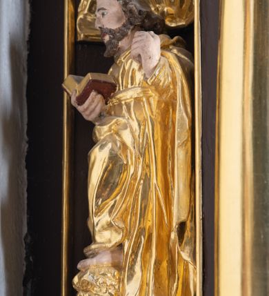Zdjęcie nr 14: Ambona drewniana, przyścienna, wisząca, dostawiona do północnej ściany nawy ze schodkami biegnącymi wzdłuż ściany. Kosz ambony jest sześcioboczny, z niewielkim parapetem. Jego boki zostały podzielone na pola stojącymi na wysokich cokołach pięcioma kolumienkami o korynckich kapitelach, dźwigających profilowane belkowanie. W polach prostokątne płyciny z konchowymi wnękami ozdobionymi muszlami z figurami ewangelistów. 
We wnękach rzeźby z przedstawieniami ewangelistów i Chrystusa. Figury drewniane pełnoplastyczne, wydrążone od tyłu, polichromowane, złocone i srebrzone, ustawione na niewielkich prostokątnych podstawach, od lewej: św. Łukasz wsparty prawą nogą na głowie byka, św. Marek wsparty prawą nogą na głowie lwa, św. Jan z orłem przy prawej nodze, Chrystus Salvator Mundi, św. Mateusz z aniołem przy prawej nodze. Ewangeliści trzymają w prawych dłoniach otwarte księgi, z wyjątkiem św. Mateusza, trzymającego kodeks w lewej ręce. Dłonie ewangelistów nieproporcjonalnie duże. Szaty bogato pofałdowane, głęboko cięte. 
Podstawa kosza bogato profilowana, ozdobiona podwieszoną dekoracyjną szyszką. Schodki ograniczone parapetem z trzema romboidalnymi płycinami w złoconych profilowanych obramieniach. Na filarze przy wejściu na schodki złocona kula z szyszką. Zaplecek w kształcie stojącego prostokąta, w górnej części ujęty zwężającymi się ku dołowi pilastrami wypełnionymi cekinami, zwieńczonymi rombowymi wypustkami i korynckimi kapitelami, które podtrzymują przełamujące się nad nimi belkowanie. Pośrodku zaplecka w prostokątnym obramieniu zamkniętym nadwieszonym łukiem półkolistym płaskorzeźbione popiersie Boga Ojca wyłaniającego się z obłoków. Prawa ręka Boga wzniesiona w geście błogosławieństwa, lewa oparta na globie ziemskim zwieńczonym krzyżem. Tłem dla postaci Boga Ojca jest rozwiana poła płaszcza układająca się niemal półkoliście. Baldachim ośmioboczny. W profilowanym podniebiu, ozdobionym pasem ornamentu małżowinowo-chrząstkowego i profilowanymi wisiorami, gołębica Ducha Świętego na tle glorii utworzonej z prostych promieni o równej długości. Baldachim ozdobiony zamkniętą koroną, którą tworzy pięć esownic pokrytych pasami ornamentu małżowinowo-chrząstkowego. W zwieńczeniu pełnoplastyczna rzeźba przedstawiająca św. Jana Chrzciciela. Figura drewniana, wydrążona z tyłu, polichromowana, złocona i srebrzona, ustawiona na niewielkiej wielobocznej profilowanej podstawie. Święty w prawej ręce trzyma wysoki krzyż, w lewej księgę, na której spoczywa Baranek Boży. Struktura ambony ciemnobrązowa. Kolumny, kapitele, pilastry w zaplecku korona baldachimu, profilowania i ornamenty złocone, z wyjątkiem srebrzonej ramy w zaplecku i gołębicy Ducha Świętego.