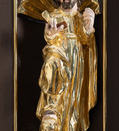 Zdjęcie nr 18: Ambona drewniana, przyścienna, wisząca, dostawiona do północnej ściany nawy ze schodkami biegnącymi wzdłuż ściany. Kosz ambony jest sześcioboczny, z niewielkim parapetem. Jego boki zostały podzielone na pola stojącymi na wysokich cokołach pięcioma kolumienkami o korynckich kapitelach, dźwigających profilowane belkowanie. W polach prostokątne płyciny z konchowymi wnękami ozdobionymi muszlami z figurami ewangelistów. 
We wnękach rzeźby z przedstawieniami ewangelistów i Chrystusa. Figury drewniane pełnoplastyczne, wydrążone od tyłu, polichromowane, złocone i srebrzone, ustawione na niewielkich prostokątnych podstawach, od lewej: św. Łukasz wsparty prawą nogą na głowie byka, św. Marek wsparty prawą nogą na głowie lwa, św. Jan z orłem przy prawej nodze, Chrystus Salvator Mundi, św. Mateusz z aniołem przy prawej nodze. Ewangeliści trzymają w prawych dłoniach otwarte księgi, z wyjątkiem św. Mateusza, trzymającego kodeks w lewej ręce. Dłonie ewangelistów nieproporcjonalnie duże. Szaty bogato pofałdowane, głęboko cięte. 
Podstawa kosza bogato profilowana, ozdobiona podwieszoną dekoracyjną szyszką. Schodki ograniczone parapetem z trzema romboidalnymi płycinami w złoconych profilowanych obramieniach. Na filarze przy wejściu na schodki złocona kula z szyszką. Zaplecek w kształcie stojącego prostokąta, w górnej części ujęty zwężającymi się ku dołowi pilastrami wypełnionymi cekinami, zwieńczonymi rombowymi wypustkami i korynckimi kapitelami, które podtrzymują przełamujące się nad nimi belkowanie. Pośrodku zaplecka w prostokątnym obramieniu zamkniętym nadwieszonym łukiem półkolistym płaskorzeźbione popiersie Boga Ojca wyłaniającego się z obłoków. Prawa ręka Boga wzniesiona w geście błogosławieństwa, lewa oparta na globie ziemskim zwieńczonym krzyżem. Tłem dla postaci Boga Ojca jest rozwiana poła płaszcza układająca się niemal półkoliście. Baldachim ośmioboczny. W profilowanym podniebiu, ozdobionym pasem ornamentu małżowinowo-chrząstkowego i profilowanymi wisiorami, gołębica Ducha Świętego na tle glorii utworzonej z prostych promieni o równej długości. Baldachim ozdobiony zamkniętą koroną, którą tworzy pięć esownic pokrytych pasami ornamentu małżowinowo-chrząstkowego. W zwieńczeniu pełnoplastyczna rzeźba przedstawiająca św. Jana Chrzciciela. Figura drewniana, wydrążona z tyłu, polichromowana, złocona i srebrzona, ustawiona na niewielkiej wielobocznej profilowanej podstawie. Święty w prawej ręce trzyma wysoki krzyż, w lewej księgę, na której spoczywa Baranek Boży. Struktura ambony ciemnobrązowa. Kolumny, kapitele, pilastry w zaplecku korona baldachimu, profilowania i ornamenty złocone, z wyjątkiem srebrzonej ramy w zaplecku i gołębicy Ducha Świętego.