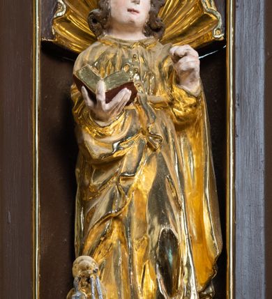 Zdjęcie nr 22: Ambona drewniana, przyścienna, wisząca, dostawiona do północnej ściany nawy ze schodkami biegnącymi wzdłuż ściany. Kosz ambony jest sześcioboczny, z niewielkim parapetem. Jego boki zostały podzielone na pola stojącymi na wysokich cokołach pięcioma kolumienkami o korynckich kapitelach, dźwigających profilowane belkowanie. W polach prostokątne płyciny z konchowymi wnękami ozdobionymi muszlami z figurami ewangelistów. 
We wnękach rzeźby z przedstawieniami ewangelistów i Chrystusa. Figury drewniane pełnoplastyczne, wydrążone od tyłu, polichromowane, złocone i srebrzone, ustawione na niewielkich prostokątnych podstawach, od lewej: św. Łukasz wsparty prawą nogą na głowie byka, św. Marek wsparty prawą nogą na głowie lwa, św. Jan z orłem przy prawej nodze, Chrystus Salvator Mundi, św. Mateusz z aniołem przy prawej nodze. Ewangeliści trzymają w prawych dłoniach otwarte księgi, z wyjątkiem św. Mateusza, trzymającego kodeks w lewej ręce. Dłonie ewangelistów nieproporcjonalnie duże. Szaty bogato pofałdowane, głęboko cięte. 
Podstawa kosza bogato profilowana, ozdobiona podwieszoną dekoracyjną szyszką. Schodki ograniczone parapetem z trzema romboidalnymi płycinami w złoconych profilowanych obramieniach. Na filarze przy wejściu na schodki złocona kula z szyszką. Zaplecek w kształcie stojącego prostokąta, w górnej części ujęty zwężającymi się ku dołowi pilastrami wypełnionymi cekinami, zwieńczonymi rombowymi wypustkami i korynckimi kapitelami, które podtrzymują przełamujące się nad nimi belkowanie. Pośrodku zaplecka w prostokątnym obramieniu zamkniętym nadwieszonym łukiem półkolistym płaskorzeźbione popiersie Boga Ojca wyłaniającego się z obłoków. Prawa ręka Boga wzniesiona w geście błogosławieństwa, lewa oparta na globie ziemskim zwieńczonym krzyżem. Tłem dla postaci Boga Ojca jest rozwiana poła płaszcza układająca się niemal półkoliście. Baldachim ośmioboczny. W profilowanym podniebiu, ozdobionym pasem ornamentu małżowinowo-chrząstkowego i profilowanymi wisiorami, gołębica Ducha Świętego na tle glorii utworzonej z prostych promieni o równej długości. Baldachim ozdobiony zamkniętą koroną, którą tworzy pięć esownic pokrytych pasami ornamentu małżowinowo-chrząstkowego. W zwieńczeniu pełnoplastyczna rzeźba przedstawiająca św. Jana Chrzciciela. Figura drewniana, wydrążona z tyłu, polichromowana, złocona i srebrzona, ustawiona na niewielkiej wielobocznej profilowanej podstawie. Święty w prawej ręce trzyma wysoki krzyż, w lewej księgę, na której spoczywa Baranek Boży. Struktura ambony ciemnobrązowa. Kolumny, kapitele, pilastry w zaplecku korona baldachimu, profilowania i ornamenty złocone, z wyjątkiem srebrzonej ramy w zaplecku i gołębicy Ducha Świętego.