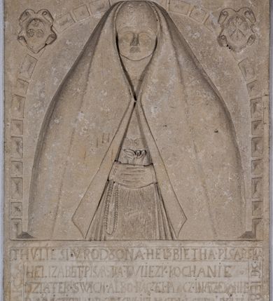 Zdjęcie nr 8: Nagrobek w formie płaskorzeźbionej tablicy o kształcie stojącego prostokąta. W jego górnej części znajduje się wyobrażenie Elżbiety z Giebułtowskich Pisarskiej przedstawionej frontalnie, do pasa. Kobieta jest obramiona półkolistą arkadą utworzoną z kaboszonów. Po bokach arkady dwa ozdobione rollwerkami kartusze z godłami herbów Bersten (po lewej stronie) i Jelita (po prawej stronie). Wyłaniająca się spod szat twarz zmarłej o kształcie sercowatym, z pełnymi policzkami z dużymi zamkniętymi oczami, z prostym, wydatnym nosem, wąskimi ustami i wyraźnie zaznaczonym podbródkiem. Zmarła jest ubrana we wdowi welon (rańtuch) spięty pod brodą i rozchylający się od środka na boki. Gładki welon zdobi jedna rurkowata fałda biegnąca na całej jego długości. Głowę nakrywa czepek, a szyję zasłania podwika. Spódnica spięta pasem z ozdobnymi klamrami, układana w drobne rurkowate fałdy. Ręce złożone, w nich chustka, przez prawą rękę przewieszony różaniec. W dolnej partii nagrobka inskrypcja kuta majuskułą. Treść inskrypcji w otoku bordiury i w polu. Inskrypcja w otoku: Inskrypcja na bordiurze "THU. LIESI. URODZONA. HELZBIETHA. PISARSKA / Z GIEBVLTOWA. KTORA MAIANCZ WIEKU / SWEGO. LIATTH. LVI. S. STHEM. SZWIATHEM. / ROZL/ONCZONA. W ROKV. 1576. XX. DNIA MARCEA." Inskrypcja w polu: "HELIZABET. PISARSKA. TV LIEZY. KOCHANIE. / DZIATEK. SWICH. ALBO. RACZEI. BACZ. I NARZEKANIE / POMNICZIE. NA. POBOŻNE. SWOIEI. MATKI SPRAWY/CZNE POTOMSTWO IAKO I IEI W TIM. BIŁ BOG. ŁASKAWY / THA WAM W BOIZNIE I BOZEJ. WYCHOWANIE DAŁA / THAKOWE. ZE. THAM. ZADNA. ZMAZA. NIEZOSTAŁA / THEGOSZ. I. PO. SMIERCZI. SWEI. VPRZYIMIE WAM. ZICZI. / BISZCIE. TAK. IAKO. ONA. DOKONALI. WSISCZI. / WIEKOW. SWOICH. A W TIM. WAM WĄTPICZ NIEPOTRZEBA. / ZE. WAS. THIM. CZIESICZ. BENDZIE. NAIWISI. BOG. Z NIEBA. / I. TIM. WAM. TO. ZAPLACZI. ZE. DNIA. OSTATNIEGO. / STANIECZIE. NAPRAWICZI. Z WIBRANEMI. IEGO. / BARBARA TOMASOWSKA. TEN. KAMIEŃ. POSTAWICZ. DAŁA". 


