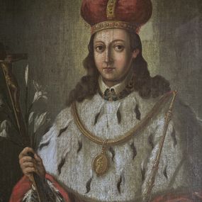 Zdjęcie nr 1: Obraz w kształcie stojącego prostokąta, w szerokiej, drewnianej ramie. Święty jest ukazany frontalnie, do kolan, w pozycji stojącej. Jego głowa jest mała, twarz owalna, oczy duże, okrągłe z wyraźnie zarysowanymi powiekami, wzrok skierowany na widza, nos prosty, usta małe. Twarz jest okolona długimi swobodnie spadającymi na ramiona pofalowanymi włosami. Głowę nakrywa mitra książęca w kolorze czerwonym, ze złotymi kabłąkami wysadzanymi kamieniami. Wokół głowy nieznacznie zaznaczony świetlisty nimb. Święty odziany jest w czerwony płaszcz podbity gronostajami, układający się dwiema pionowymi fałdami wokół wysuwających się spod płaszcza rąk. W prawej ręce trzyma krucyfiks i lilie, w lewej, opuszczonej nieco niżej dzierży berło. Na ramionach gronostajowa peleryna z brzegiem zaznaczonym lamówką i zawieszony na złotym łańcuchu owalny medalion z wizerunkiem Matki Boskiej z Dzieciątkiem, ponad pelerynką widoczny fragment spodniej szaty i kołnierzyk. Tło obrazu jednolite w kolorze brązowo-szarym.