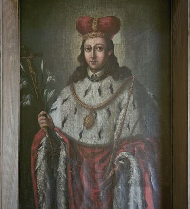Zdjęcie nr 5: Obraz w kształcie stojącego prostokąta, w szerokiej, drewnianej ramie. Święty jest ukazany frontalnie, do kolan, w pozycji stojącej. Jego głowa jest mała, twarz owalna, oczy duże, okrągłe z wyraźnie zarysowanymi powiekami, wzrok skierowany na widza, nos prosty, usta małe. Twarz jest okolona długimi swobodnie spadającymi na ramiona pofalowanymi włosami. Głowę nakrywa mitra książęca w kolorze czerwonym, ze złotymi kabłąkami wysadzanymi kamieniami. Wokół głowy nieznacznie zaznaczony świetlisty nimb. Święty odziany jest w czerwony płaszcz podbity gronostajami, układający się dwiema pionowymi fałdami wokół wysuwających się spod płaszcza rąk. W prawej ręce trzyma krucyfiks i lilie, w lewej, opuszczonej nieco niżej dzierży berło. Na ramionach gronostajowa peleryna z brzegiem zaznaczonym lamówką i zawieszony na złotym łańcuchu owalny medalion z wizerunkiem Matki Boskiej z Dzieciątkiem, ponad pelerynką widoczny fragment spodniej szaty i kołnierzyk. Tło obrazu jednolite w kolorze brązowo-szarym.
