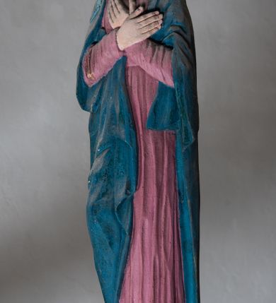 Zdjęcie nr 5: Rzeźba drewniana, pełnoplastyczna, polichromowana przedstawia Matkę Boską stojącą na niewielkim postumencie w kształcie zbliżonym do połowy sfery. Matka Boska ukazana w pozycji stojącej, frontalnie, w lekkim kontrapoście, z ciałem lekko zwróconym w kierunku krzyża, z rękoma skrzyżowanymi na piersi. Jej głowa jest nakryta welonem. Twarz ma owalną, oczy z opadającymi kącikami, nos prosty, a usta małe. Maria ubrana w długą suknię w kolorze zgaszonego różu przepasaną w stanie oraz niebieski płaszcz narzucony na ramiona  i opływający sylwetkę, na szyi udrapowana chusta. Fałdy szaty pionowe, płytkie, układające się miękko.