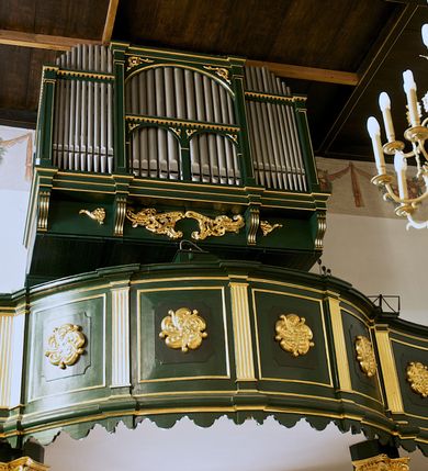 Zdjęcie nr 17: Chór muzyczny na zachodniej ścianie nawy, wsparty na dwóch słupach, ozdobionych od strony nawy dwoma kanelowanymi pilastrami o kapitelach kompozytowych. Jego parapet jest wklęsło-wypukły, z profilowanym cokołem, podzielony na kwatery kanelowanymi i złoconymi pilastrami. W kwaterach wypukłe pola kwadratowe o ćwierkolistych narożach ozdobione rzeźbionymi stylizowanymi rozetami. Parapet zwieńczony niewielkim gzymsem przełamanym na osi pilastrów. Pod listwą cokołu falisty fartuch. Struktura chóru muzycznego ciemnozielona. Pola płycin oliwkowo-ciemnozielone. Pilasty, rozety i profilowania są złocone. 
Znajdujący się na chórze prospekt wsparty na cokole z czterema kroksztynami, trzyosiowy, z osiami wydzielonymi kwadratowymi w podstawie filarkami. Oś środkowa podzielona na wie strefy: dolną z dwiema arkadkami z kostkowanym gzymsem i górną zamkniętą łukiem odcinkowym. Osie boczne zakończone gzymsem z kostkowaniem. W partii cokołowej bogato rzeźbiony motyw małżowinowo-chrząstkowy. 