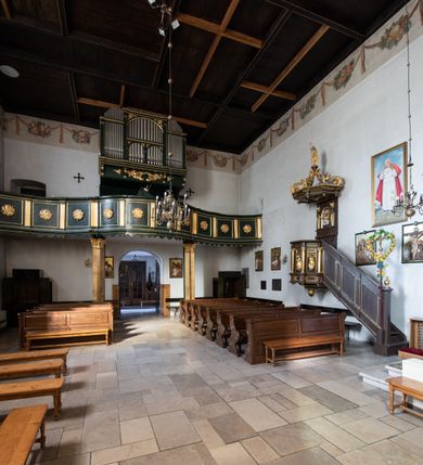 Zdjęcie nr 20: Chór muzyczny na zachodniej ścianie nawy, wsparty na dwóch słupach, ozdobionych od strony nawy dwoma kanelowanymi pilastrami o kapitelach kompozytowych. Jego parapet jest wklęsło-wypukły, z profilowanym cokołem, podzielony na kwatery kanelowanymi i złoconymi pilastrami. W kwaterach wypukłe pola kwadratowe o ćwierkolistych narożach ozdobione rzeźbionymi stylizowanymi rozetami. Parapet zwieńczony niewielkim gzymsem przełamanym na osi pilastrów. Pod listwą cokołu falisty fartuch. Struktura chóru muzycznego ciemnozielona. Pola płycin oliwkowo-ciemnozielone. Pilasty, rozety i profilowania są złocone. 
Znajdujący się na chórze prospekt wsparty na cokole z czterema kroksztynami, trzyosiowy, z osiami wydzielonymi kwadratowymi w podstawie filarkami. Oś środkowa podzielona na wie strefy: dolną z dwiema arkadkami z kostkowanym gzymsem i górną zamkniętą łukiem odcinkowym. Osie boczne zakończone gzymsem z kostkowaniem. W partii cokołowej bogato rzeźbiony motyw małżowinowo-chrząstkowy. 