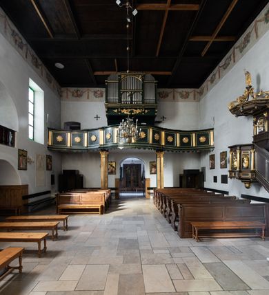 Zdjęcie nr 21: Chór muzyczny na zachodniej ścianie nawy, wsparty na dwóch słupach, ozdobionych od strony nawy dwoma kanelowanymi pilastrami o kapitelach kompozytowych. Jego parapet jest wklęsło-wypukły, z profilowanym cokołem, podzielony na kwatery kanelowanymi i złoconymi pilastrami. W kwaterach wypukłe pola kwadratowe o ćwierkolistych narożach ozdobione rzeźbionymi stylizowanymi rozetami. Parapet zwieńczony niewielkim gzymsem przełamanym na osi pilastrów. Pod listwą cokołu falisty fartuch. Struktura chóru muzycznego ciemnozielona. Pola płycin oliwkowo-ciemnozielone. Pilasty, rozety i profilowania są złocone. 
Znajdujący się na chórze prospekt wsparty na cokole z czterema kroksztynami, trzyosiowy, z osiami wydzielonymi kwadratowymi w podstawie filarkami. Oś środkowa podzielona na wie strefy: dolną z dwiema arkadkami z kostkowanym gzymsem i górną zamkniętą łukiem odcinkowym. Osie boczne zakończone gzymsem z kostkowaniem. W partii cokołowej bogato rzeźbiony motyw małżowinowo-chrząstkowy. 