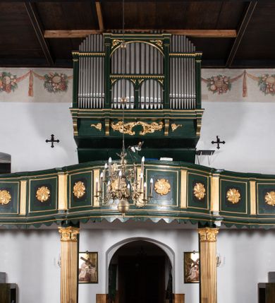 Zdjęcie nr 22: Chór muzyczny na zachodniej ścianie nawy, wsparty na dwóch słupach, ozdobionych od strony nawy dwoma kanelowanymi pilastrami o kapitelach kompozytowych. Jego parapet jest wklęsło-wypukły, z profilowanym cokołem, podzielony na kwatery kanelowanymi i złoconymi pilastrami. W kwaterach wypukłe pola kwadratowe o ćwierkolistych narożach ozdobione rzeźbionymi stylizowanymi rozetami. Parapet zwieńczony niewielkim gzymsem przełamanym na osi pilastrów. Pod listwą cokołu falisty fartuch. Struktura chóru muzycznego ciemnozielona. Pola płycin oliwkowo-ciemnozielone. Pilasty, rozety i profilowania są złocone. 
Znajdujący się na chórze prospekt wsparty na cokole z czterema kroksztynami, trzyosiowy, z osiami wydzielonymi kwadratowymi w podstawie filarkami. Oś środkowa podzielona na wie strefy: dolną z dwiema arkadkami z kostkowanym gzymsem i górną zamkniętą łukiem odcinkowym. Osie boczne zakończone gzymsem z kostkowaniem. W partii cokołowej bogato rzeźbiony motyw małżowinowo-chrząstkowy. 