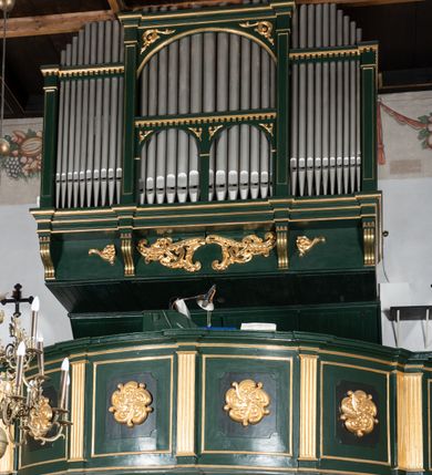 Zdjęcie nr 4: Chór muzyczny na zachodniej ścianie nawy, wsparty na dwóch słupach, ozdobionych od strony nawy dwoma kanelowanymi pilastrami o kapitelach kompozytowych. Jego parapet jest wklęsło-wypukły, z profilowanym cokołem, podzielony na kwatery kanelowanymi i złoconymi pilastrami. W kwaterach wypukłe pola kwadratowe o ćwierkolistych narożach ozdobione rzeźbionymi stylizowanymi rozetami. Parapet zwieńczony niewielkim gzymsem przełamanym na osi pilastrów. Pod listwą cokołu falisty fartuch. Struktura chóru muzycznego ciemnozielona. Pola płycin oliwkowo-ciemnozielone. Pilasty, rozety i profilowania są złocone. 
Znajdujący się na chórze prospekt wsparty na cokole z czterema kroksztynami, trzyosiowy, z osiami wydzielonymi kwadratowymi w podstawie filarkami. Oś środkowa podzielona na wie strefy: dolną z dwiema arkadkami z kostkowanym gzymsem i górną zamkniętą łukiem odcinkowym. Osie boczne zakończone gzymsem z kostkowaniem. W partii cokołowej bogato rzeźbiony motyw małżowinowo-chrząstkowy. 