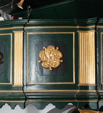 Zdjęcie nr 16: Chór muzyczny na zachodniej ścianie nawy, wsparty na dwóch słupach, ozdobionych od strony nawy dwoma kanelowanymi pilastrami o kapitelach kompozytowych. Jego parapet jest wklęsło-wypukły, z profilowanym cokołem, podzielony na kwatery kanelowanymi i złoconymi pilastrami. W kwaterach wypukłe pola kwadratowe o ćwierkolistych narożach ozdobione rzeźbionymi stylizowanymi rozetami. Parapet zwieńczony niewielkim gzymsem przełamanym na osi pilastrów. Pod listwą cokołu falisty fartuch. Struktura chóru muzycznego ciemnozielona. Pola płycin oliwkowo-ciemnozielone. Pilasty, rozety i profilowania są złocone. 
Znajdujący się na chórze prospekt wsparty na cokole z czterema kroksztynami, trzyosiowy, z osiami wydzielonymi kwadratowymi w podstawie filarkami. Oś środkowa podzielona na wie strefy: dolną z dwiema arkadkami z kostkowanym gzymsem i górną zamkniętą łukiem odcinkowym. Osie boczne zakończone gzymsem z kostkowaniem. W partii cokołowej bogato rzeźbiony motyw małżowinowo-chrząstkowy. 