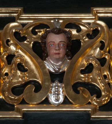 Zdjęcie nr 35: Ołtarz architektoniczny, na wysokim cokole, jednokondygnacyjny, trójosiowy, ze zwieńczeniem; osie wyznaczone umieszczonymi na wysokich cokołach kolumnami o kapitelach kompozytowych, podtrzymującymi występujące nad podporami uproszczone belkowanie i gzyms, ponad nimi trójkątny, przerywany przyczółek. W strefie dolnej, w osiach skrajnych, po bokach mensy bramki zamknięte półkoliście, służące do obejścia ołtarza. Mensa prostopadłościenna, o profilowanym obramieniu antependium i z profilowanymi prostokątnymi płycinami na bokach. Powyżej, w pierwszej kondygnacji, w osiach skrajnych nisze zamknięte łukiem półkolistym z konchami muszlowymi, w osi środkowej prostokątna wnęka na obraz ołtarzowy. Płyciny na cokołach, powyżej półkolistych wnęk oraz na predelli ażurowe, w kształcie prostokąta z uszakami. Zwieńczenie jednoosiowe, flankowane kolumienkami o kapitelach kompozytowych, z występującym nad podporami belkowaniem i gzymsem oraz półkolistym przerywanym przyczółkiem. W polu środkowym owalna profilowana nisza na obraz, ponad którą w szczycie ołtarza gloria promienista. Nastawa flankowana uszakami w z motywów ornamentu małżowinowo-chrząstkowego. Belkowanie, profilowane, prostokątne pole na obraz, predella oraz płyciny na cokołach i powyżej półkolistych wnęk, wypełnione ornamentem małżowinowo-chrząstkowym. Powyżej bramek w części cokołowej podwieszone girlandy. W zwieńczeniu małżowinowo-chrząstkowe uszaki oraz płyciny wypełnione ornamentem małżowinowo-chrząstkowym. W narożach stylizowane liście. Profilowana wnęka na obraz w zwieńczeniu  wypełniona lilijkami. Kolumny, gzymsy i profilowania otworów złocone. Gloria promienista z puttami oraz Okiem Opatrzności na tle trójkąta równobocznego. Antepedium ozdobione romboidalną siatką, w narożach wstęga regencyjna przechodząca w akant. Pośrodku litery IHS w glorii promienistej. W płycinach na cokołach i powyżej wnęk główki puttów. W niszach rzeźby św. Wojciecha i św. Stanisława. W centralnym polu obraz z przedstawieniem św. Grzegorza Wielkiego, w zwieńczeniu Wniebowzięcie Najświętszej Marii Panny. Na przerywanym przyczółku nastawy rzeźby aniołów. Rzeźba anioła po lewej stronie, pełna, całopostaciowa. Anioł ukazany w pozycji półleżącej, w trzech czwartych, z lewą nogą wysuniętą i wzniesioną głową. Ręce ugięte w łokciach i uniesione. Twarz pociągła, włosy ciemne, kręcone, sięgające do ramion i odsłaniające uszy. Anioł odziany jest w długą, złotą suknię, z podwiniętymi rękawami i odsłaniającą lewą nogę. Fałdy głęboko rzeźbione, na kształt litery V i pionowych rurek.Rzeźba anioła po prawej, pełna, całopostaciowa. Anioł ukazany w pozycji półleżącej, w trzech czwartych, z lewą nogą wysuniętą i wzniesioną głową. Lewa ręka ugięta w łokciu i ułożona na piersi, prawa wyprostowana. Twarz pociągła, włosy ciemne, kręcone, sięgające do ramion i odsłaniające uszy. Anioł ubrany w długą, złotą suknię, z podwiniętymi rękawami i odsłaniającą lewą nogę. Fałdy głęboko rzeźbione, na kształt litery V i pionowych rurek.