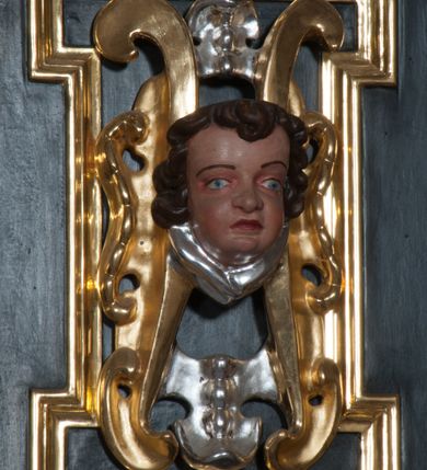 Zdjęcie nr 32: Ołtarz architektoniczny, na wysokim cokole, jednokondygnacyjny, trójosiowy, ze zwieńczeniem; osie wyznaczone umieszczonymi na wysokich cokołach kolumnami o kapitelach kompozytowych, podtrzymującymi występujące nad podporami uproszczone belkowanie i gzyms, ponad nimi trójkątny, przerywany przyczółek. W strefie dolnej, w osiach skrajnych, po bokach mensy bramki zamknięte półkoliście, służące do obejścia ołtarza. Mensa prostopadłościenna, o profilowanym obramieniu antependium i z profilowanymi prostokątnymi płycinami na bokach. Powyżej, w pierwszej kondygnacji, w osiach skrajnych nisze zamknięte łukiem półkolistym z konchami muszlowymi, w osi środkowej prostokątna wnęka na obraz ołtarzowy. Płyciny na cokołach, powyżej półkolistych wnęk oraz na predelli ażurowe, w kształcie prostokąta z uszakami. Zwieńczenie jednoosiowe, flankowane kolumienkami o kapitelach kompozytowych, z występującym nad podporami belkowaniem i gzymsem oraz półkolistym przerywanym przyczółkiem. W polu środkowym owalna profilowana nisza na obraz, ponad którą w szczycie ołtarza gloria promienista. Nastawa flankowana uszakami w z motywów ornamentu małżowinowo-chrząstkowego. Belkowanie, profilowane, prostokątne pole na obraz, predella oraz płyciny na cokołach i powyżej półkolistych wnęk, wypełnione ornamentem małżowinowo-chrząstkowym. Powyżej bramek w części cokołowej podwieszone girlandy. W zwieńczeniu małżowinowo-chrząstkowe uszaki oraz płyciny wypełnione ornamentem małżowinowo-chrząstkowym. W narożach stylizowane liście. Profilowana wnęka na obraz w zwieńczeniu  wypełniona lilijkami. Kolumny, gzymsy i profilowania otworów złocone. Gloria promienista z puttami oraz Okiem Opatrzności na tle trójkąta równobocznego. Antepedium ozdobione romboidalną siatką, w narożach wstęga regencyjna przechodząca w akant. Pośrodku litery IHS w glorii promienistej. W płycinach na cokołach i powyżej wnęk główki puttów. W niszach rzeźby św. Wojciecha i św. Stanisława. W centralnym polu obraz z przedstawieniem św. Grzegorza Wielkiego, w zwieńczeniu Wniebowzięcie Najświętszej Marii Panny. Na przerywanym przyczółku nastawy rzeźby aniołów. Rzeźba anioła po lewej stronie, pełna, całopostaciowa. Anioł ukazany w pozycji półleżącej, w trzech czwartych, z lewą nogą wysuniętą i wzniesioną głową. Ręce ugięte w łokciach i uniesione. Twarz pociągła, włosy ciemne, kręcone, sięgające do ramion i odsłaniające uszy. Anioł odziany jest w długą, złotą suknię, z podwiniętymi rękawami i odsłaniającą lewą nogę. Fałdy głęboko rzeźbione, na kształt litery V i pionowych rurek.Rzeźba anioła po prawej, pełna, całopostaciowa. Anioł ukazany w pozycji półleżącej, w trzech czwartych, z lewą nogą wysuniętą i wzniesioną głową. Lewa ręka ugięta w łokciu i ułożona na piersi, prawa wyprostowana. Twarz pociągła, włosy ciemne, kręcone, sięgające do ramion i odsłaniające uszy. Anioł ubrany w długą, złotą suknię, z podwiniętymi rękawami i odsłaniającą lewą nogę. Fałdy głęboko rzeźbione, na kształt litery V i pionowych rurek.