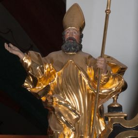 Zdjęcie nr 1: Rzeźba ścięta z tyłu, polichromowana. Święty Wojciech ukazany frontalnie, stojący w lekkim kontrapoście, ciężar ciała wspierający na lewej nodze; prawą rękę, odstawioną od boku, unosi na wysokość piersi, lewą wspiera na pastorale. Twarz okolona gęstą, długą brodą z wąsami. Święty ubrany w długie, złote, mocno fałdowane szaty. Na głowie mitra biskupia. Karnacje w kolorze naturalnym.