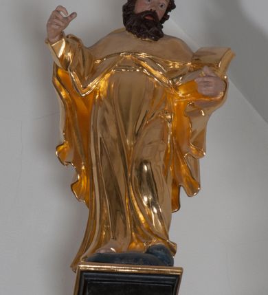 Zdjęcie nr 2: Rzeźba ścięta z tyłu, polichromowana, złocona. Święty Jakub Starszy ukazany frontalnie, w lekkim kontrapoście, ciężar ciała wspierający na prawej nodze, w lewej ręce trzyma księgę, prawą unosi na wysokość piersi. Twarz okolona czarnymi, krótkimi, kędzierzawymi włosami i zarostem. Święty ubrany w złote szaty. Tunika długa, układająca się w miękkie płytkie fałdy, płaszcz długi, spięty na piersi, okrywa ramiona i plecy. Na plecach kapelusz.