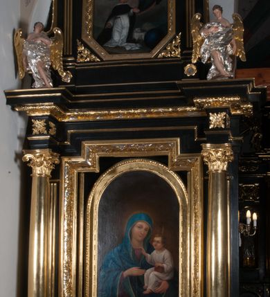Zdjęcie nr 8: Nastawa ołtarzowa architektoniczna, jednokondygnacyjna, jednoosiowa, ze zwieńczeniem. Pole środkowe flankowane kolumnami o kompozytowych kapitelach, umieszczonymi na wysokich, prostopadłościennych postumentach i dźwigającymi uproszczone belkowanie i wydatny profilowany gzyms, występujące nad podporami. Pomiędzy kolumnami prostokątna zamknięta schodkowo nisza na obraz ołtarzowy, ujęta złoconą ramą zdobioną motywami roślinnymi. W niszy obraz Matki Boskiej z Dzieciątkiem, w kształcie prostokąta zamkniętego łukiem półpełnym, ujęty w osobną gładką złoconą ramę. Postumenty pod kolumny i belkowanie ozdobiony ażurowymi złoconymi płycinami z dekoracją ornamentalną. Zwieńczenie w kształcie prostokąta zakończone profilowanym, falistym gzymsem wspartym na dwóch złoconych, kanelowanych pilastrach, ujęte po bokach spływami wolutowymi. W polu zwieńczenia ośmioboczny obraz z przedstawieniem św. Dominika odbierającego różaniec z rąk Matki Boskiej z Dzieciątkiem, w bogatej złoconej ramie. Wokół ramy obrazu ażurowe motywy ornamentalne i rozetki. Na gzymsach w osiach kolumn oraz w osi zwieńczenia rzeźby uskrzydlonych aniołów. Mensa prostopadłościenna; antependium w profilowanym obramieniu, ozdobione ukośną kratką, pośrodku splecione litery imienia Maria, w narożach motywy liści. Boki mensy ozdobione prostokątnymi płycinami. Struktura ołtarza malowana na czarno, kolumny, motywy ornamentalne i gzymsy złocone.