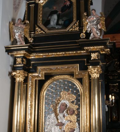 Zdjęcie nr 10: Nastawa ołtarzowa architektoniczna, jednokondygnacyjna, jednoosiowa, ze zwieńczeniem. Pole środkowe flankowane kolumnami o kompozytowych kapitelach, umieszczonymi na wysokich, prostopadłościennych postumentach i dźwigającymi uproszczone belkowanie i wydatny profilowany gzyms, występujące nad podporami. Pomiędzy kolumnami prostokątna zamknięta schodkowo nisza na obraz ołtarzowy, ujęta złoconą ramą zdobioną motywami roślinnymi. W niszy obraz Matki Boskiej z Dzieciątkiem, w kształcie prostokąta zamkniętego łukiem półpełnym, ujęty w osobną gładką złoconą ramę. Postumenty pod kolumny i belkowanie ozdobiony ażurowymi złoconymi płycinami z dekoracją ornamentalną. Zwieńczenie w kształcie prostokąta zakończone profilowanym, falistym gzymsem wspartym na dwóch złoconych, kanelowanych pilastrach, ujęte po bokach spływami wolutowymi. W polu zwieńczenia ośmioboczny obraz z przedstawieniem św. Dominika odbierającego różaniec z rąk Matki Boskiej z Dzieciątkiem, w bogatej złoconej ramie. Wokół ramy obrazu ażurowe motywy ornamentalne i rozetki. Na gzymsach w osiach kolumn oraz w osi zwieńczenia rzeźby uskrzydlonych aniołów. Mensa prostopadłościenna; antependium w profilowanym obramieniu, ozdobione ukośną kratką, pośrodku splecione litery imienia Maria, w narożach motywy liści. Boki mensy ozdobione prostokątnymi płycinami. Struktura ołtarza malowana na czarno, kolumny, motywy ornamentalne i gzymsy złocone.